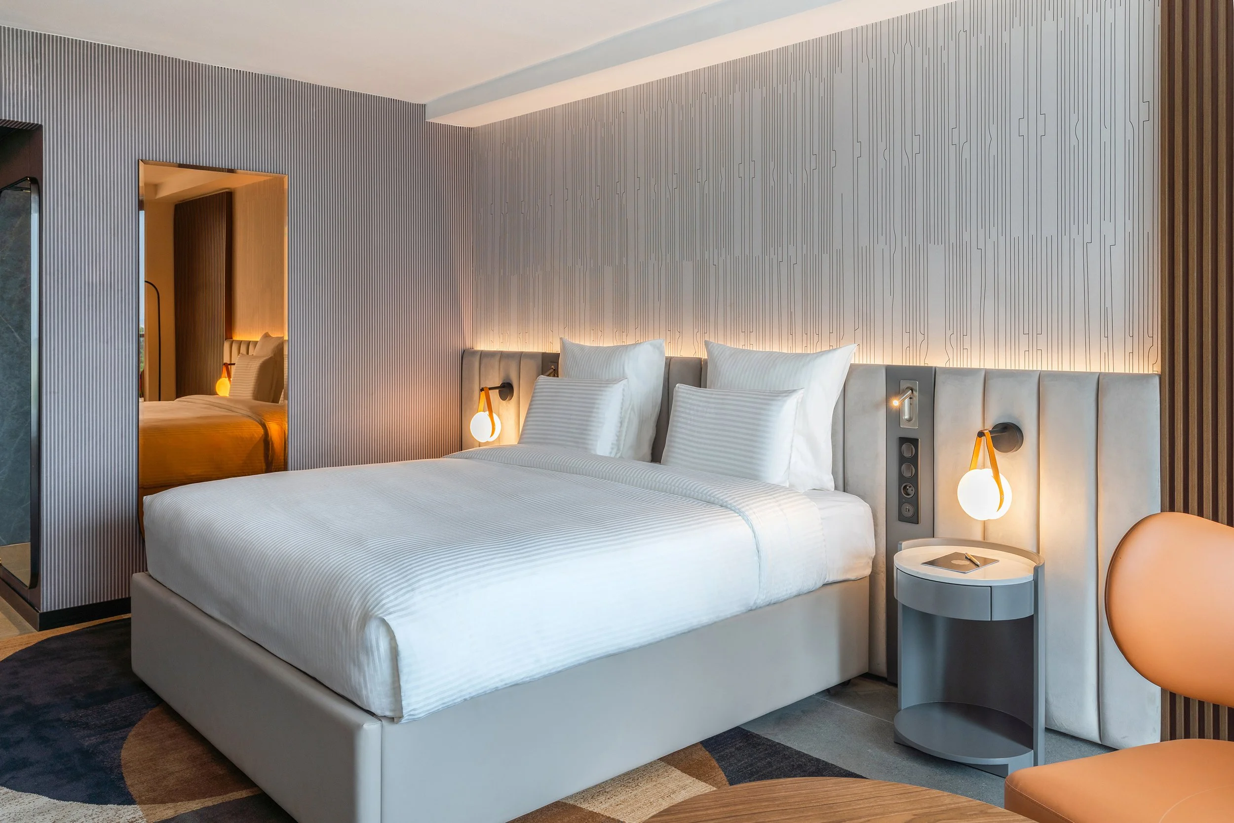 Chambre d'hôtel moderne avec lit double blanc, lampes de chevet, oreillers blancs et murs design avec éclairage indirect.