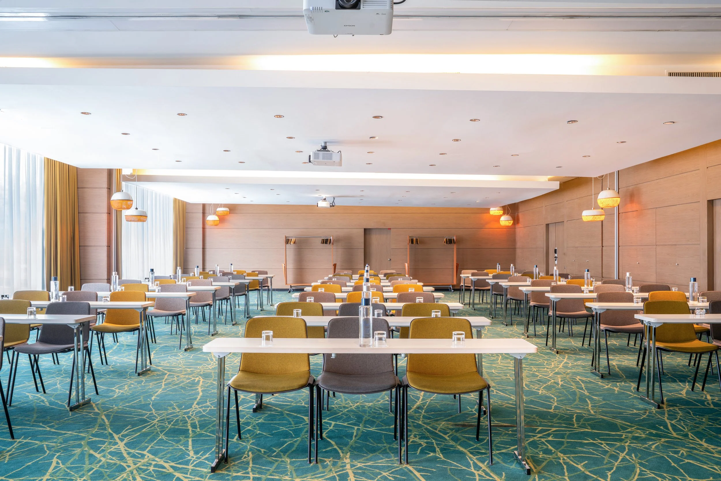 Salle de conférence en style salle de classe avec tables et chaises colorées, éclairage tamisé, murs en bois et tapis rouge, équipée pour une réunion ou un séminaire.