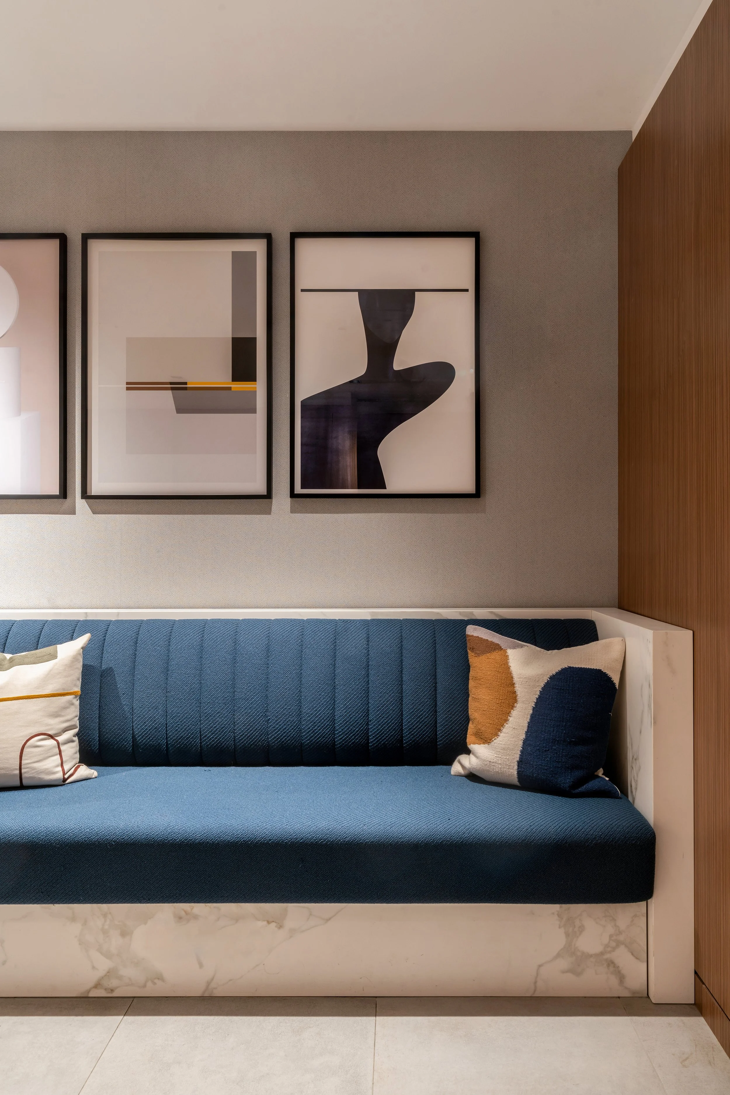 Canapé bleu avec deux coussins abstraits près d’un mur décoré de trois tableaux modernes.
