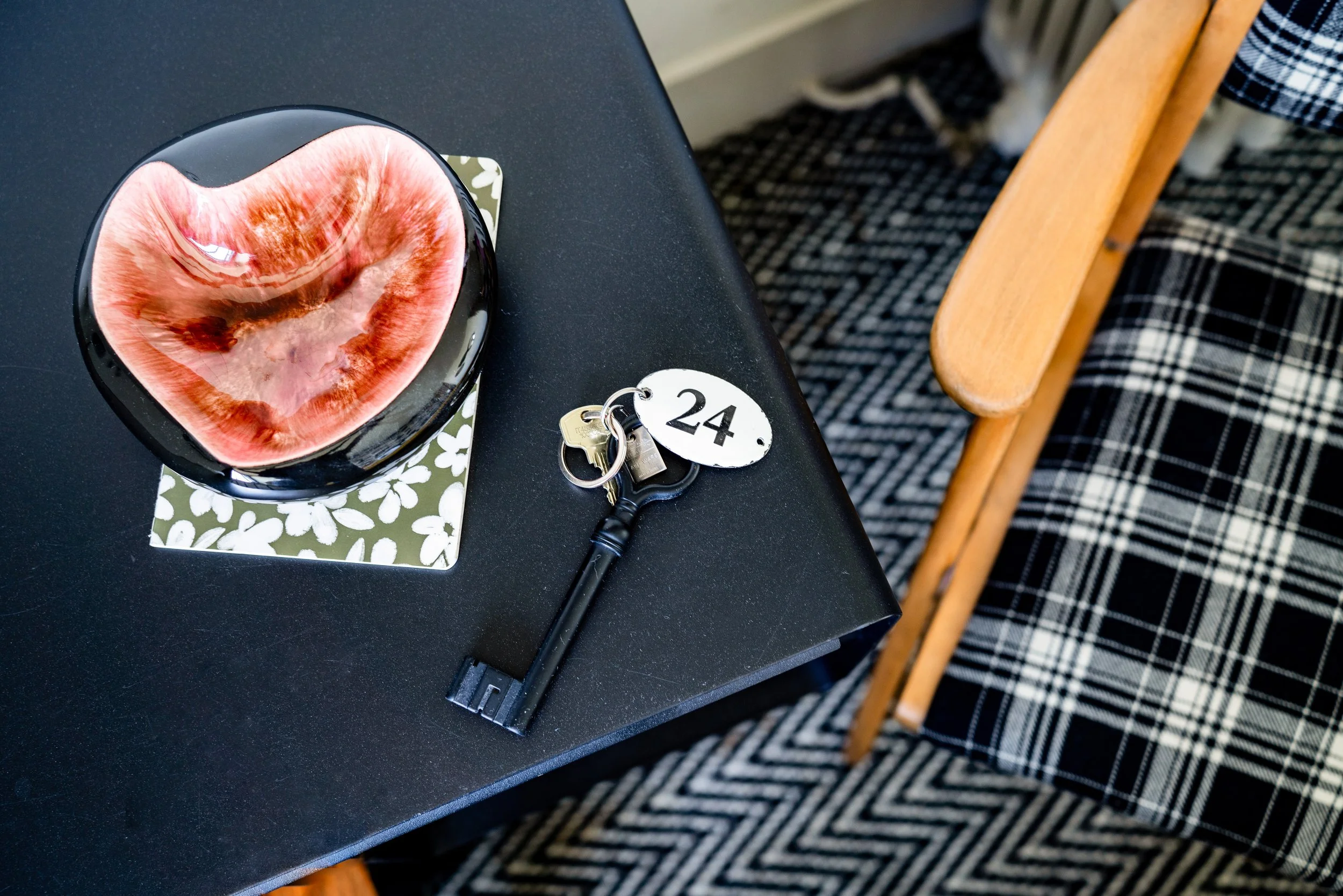 Une table noire avec un bol en forme de cœur, un set de clés avec un porte-clés numéroté 24, une chaise en bois et un tapis à motifs en noir et blanc.