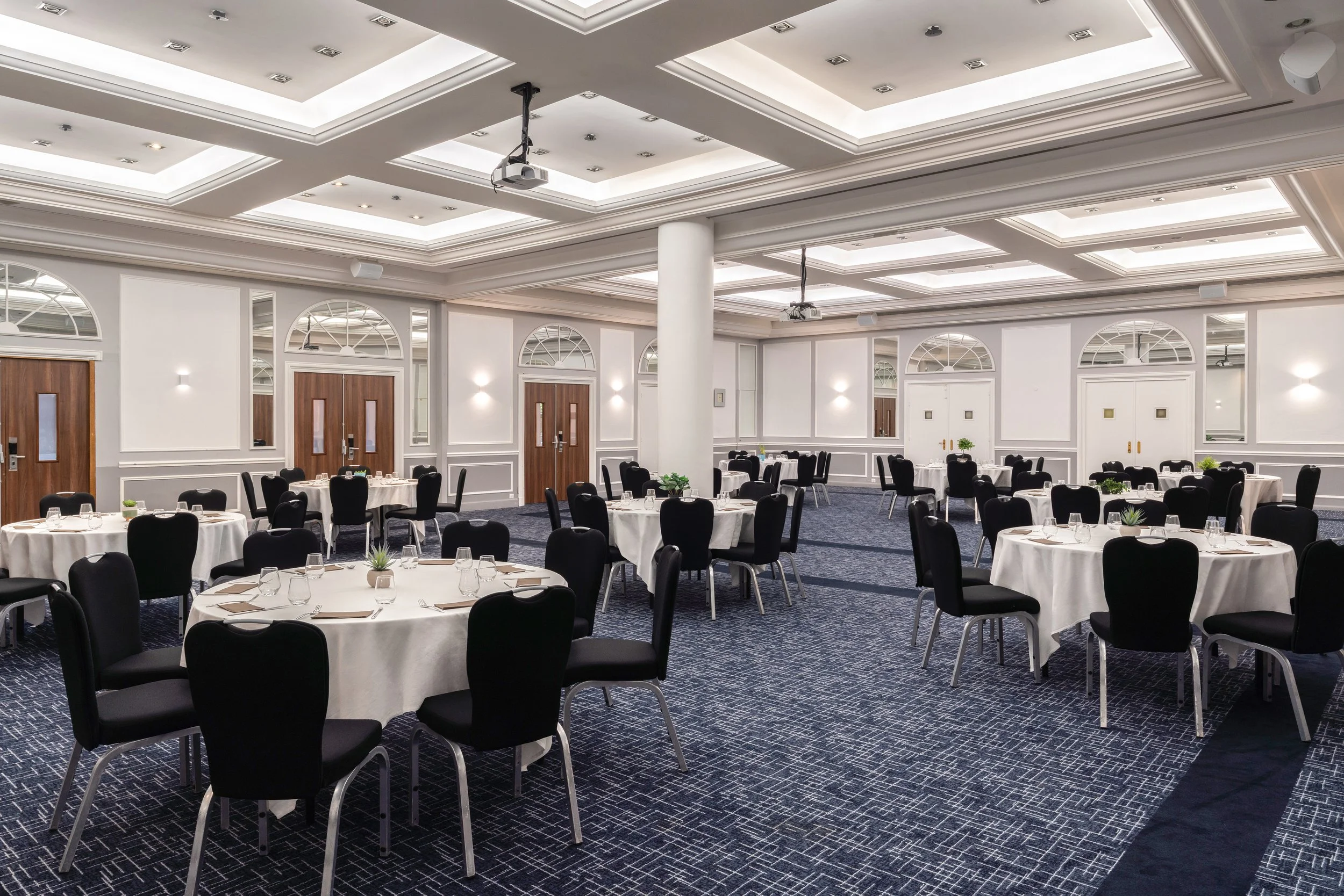 Salle de réception élégante avec des tables rondes, nappes blanches, chaises noires, décorée dans un style moderne et lumineux.