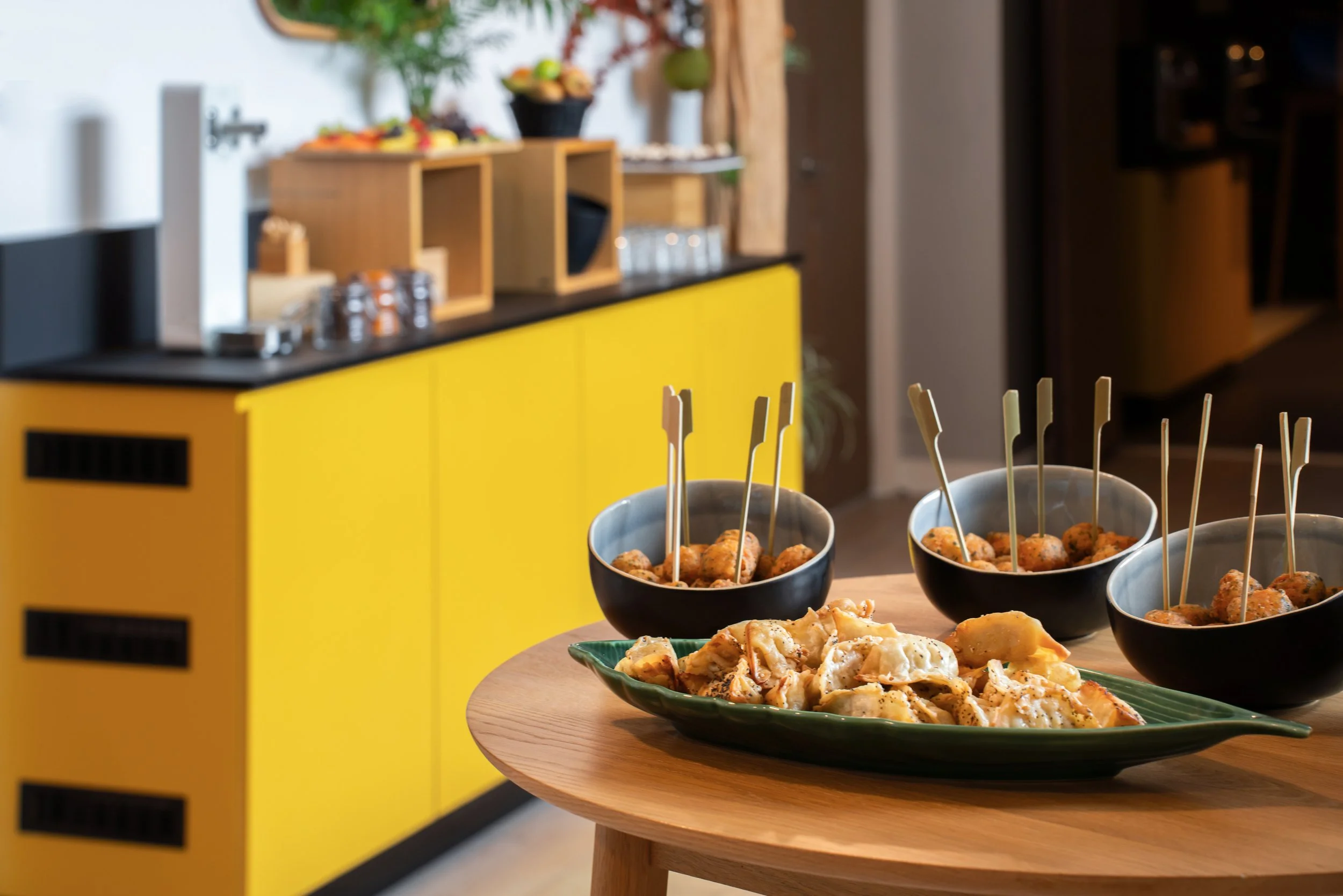 Buffet d'une pause d'un séminaire, sur une table en bois, avec un meuble jaune en arrière-plan.