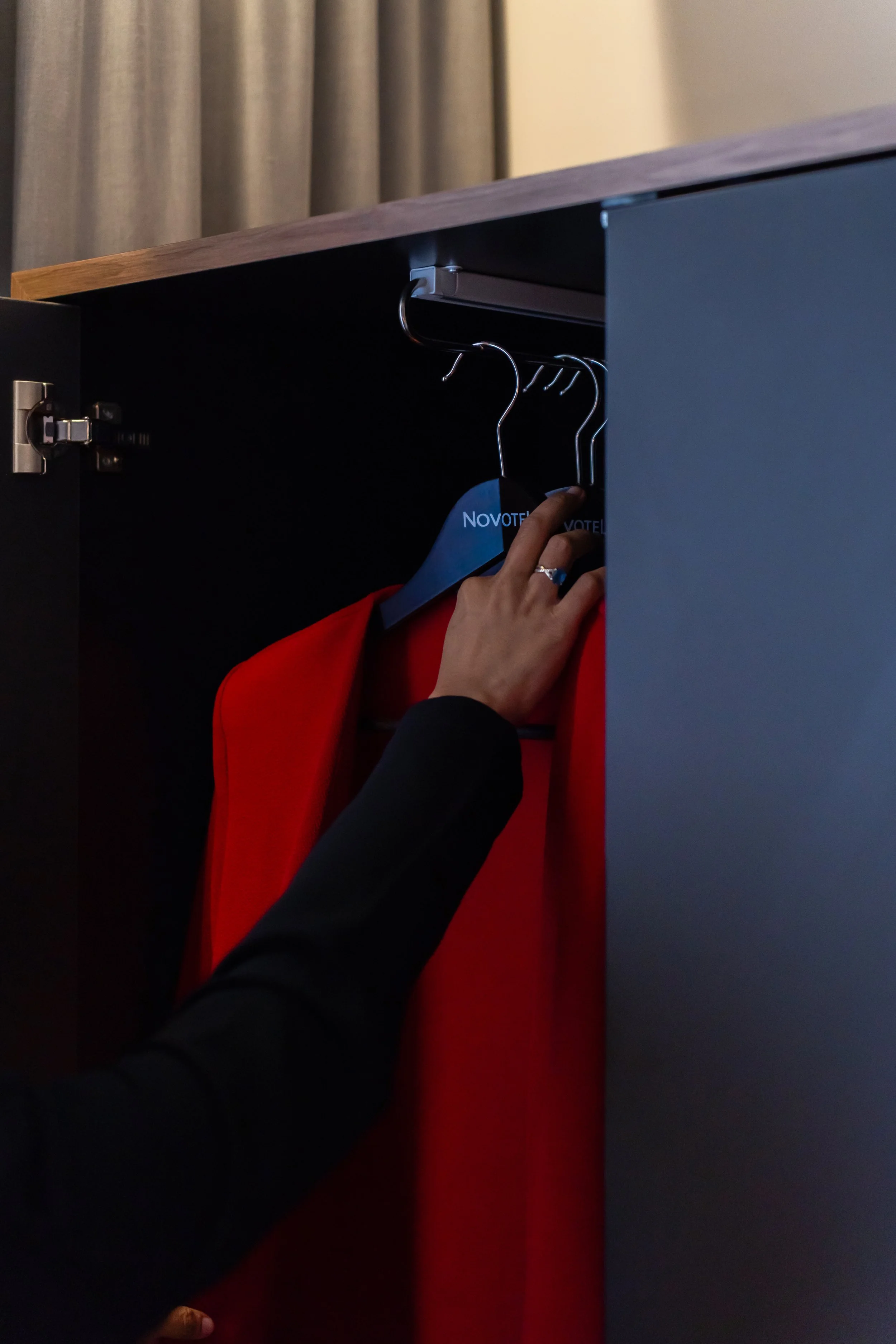 Une main enlève un cintre avec un vêtement rouge dans une armoire noire.