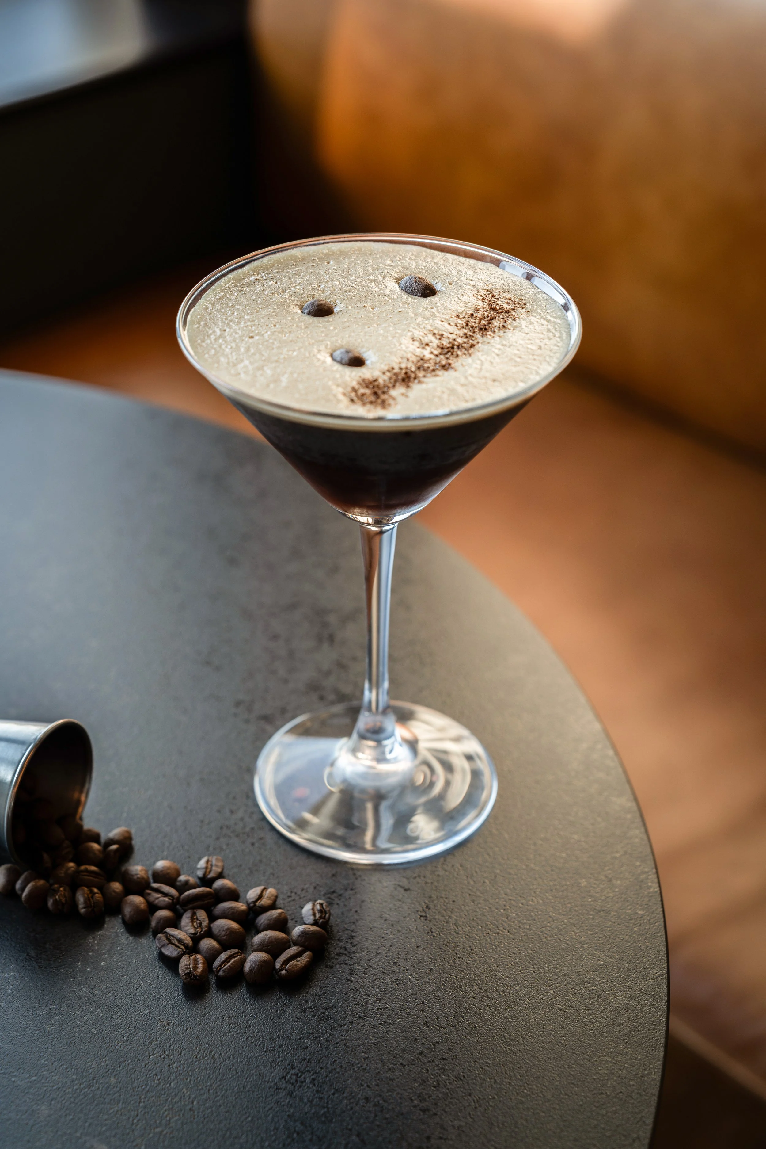 Cocktail à café noir dans un verre à martini, décoré avec de la crème et du cacao en poudre, posés sur une table avec des grains de café et une petite boîte.