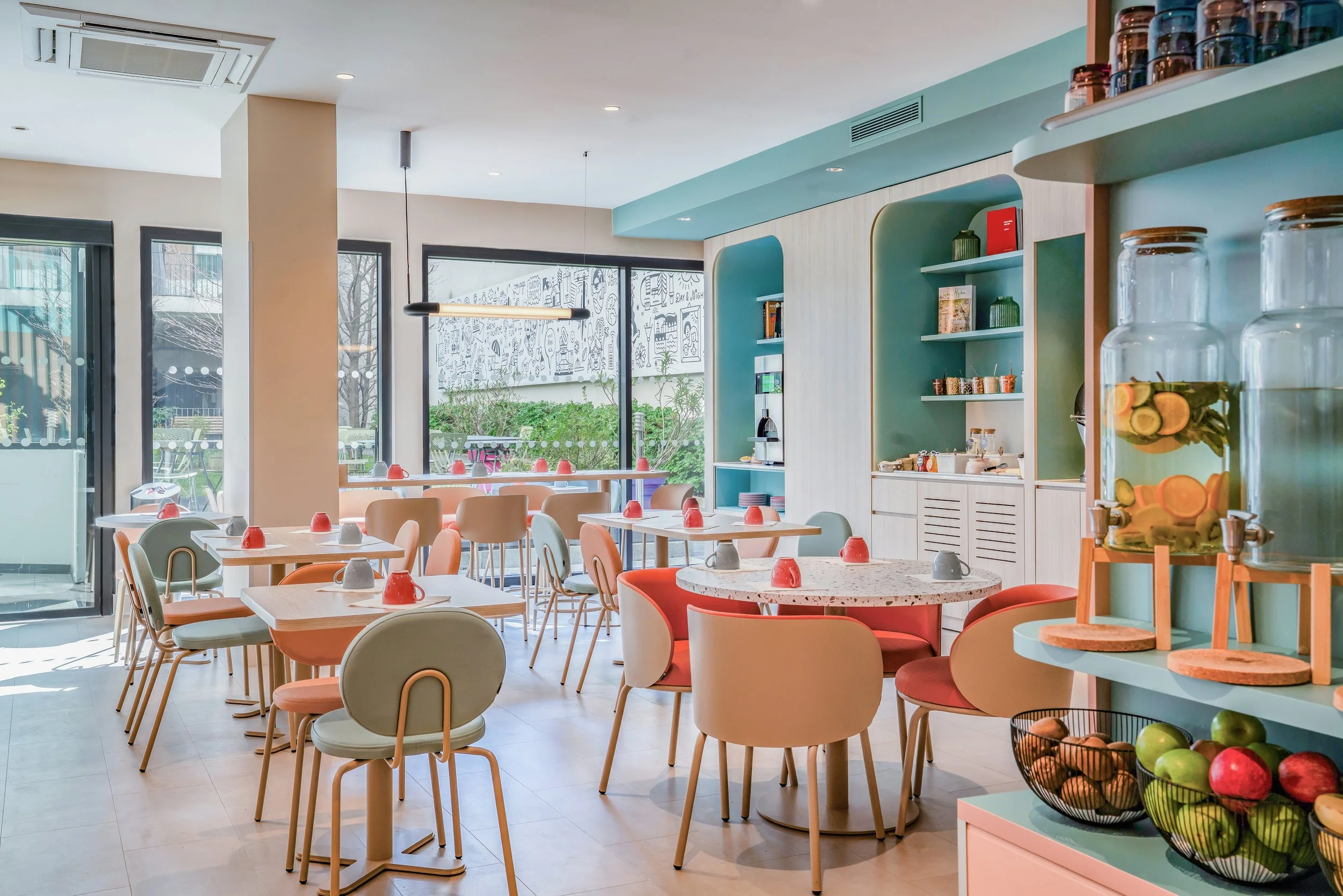 Salle de café ou de restaurant avec tables, chaises colorées, et distributeurs de fruits dans un décor lumineux et moderne.
