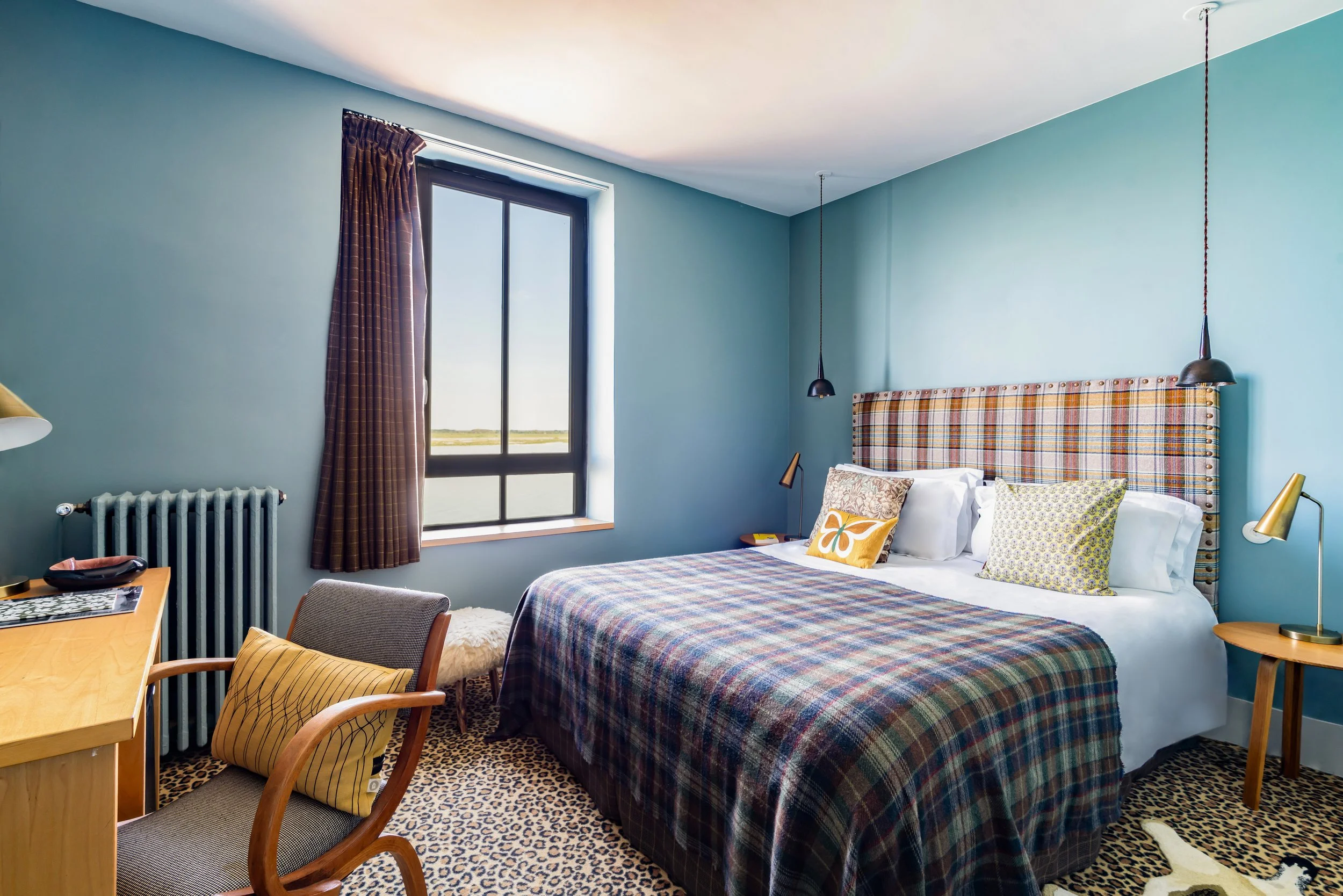 Chambre d'hôtel avec un grand lit, coussins colorés, une fenêtre et un bureau.