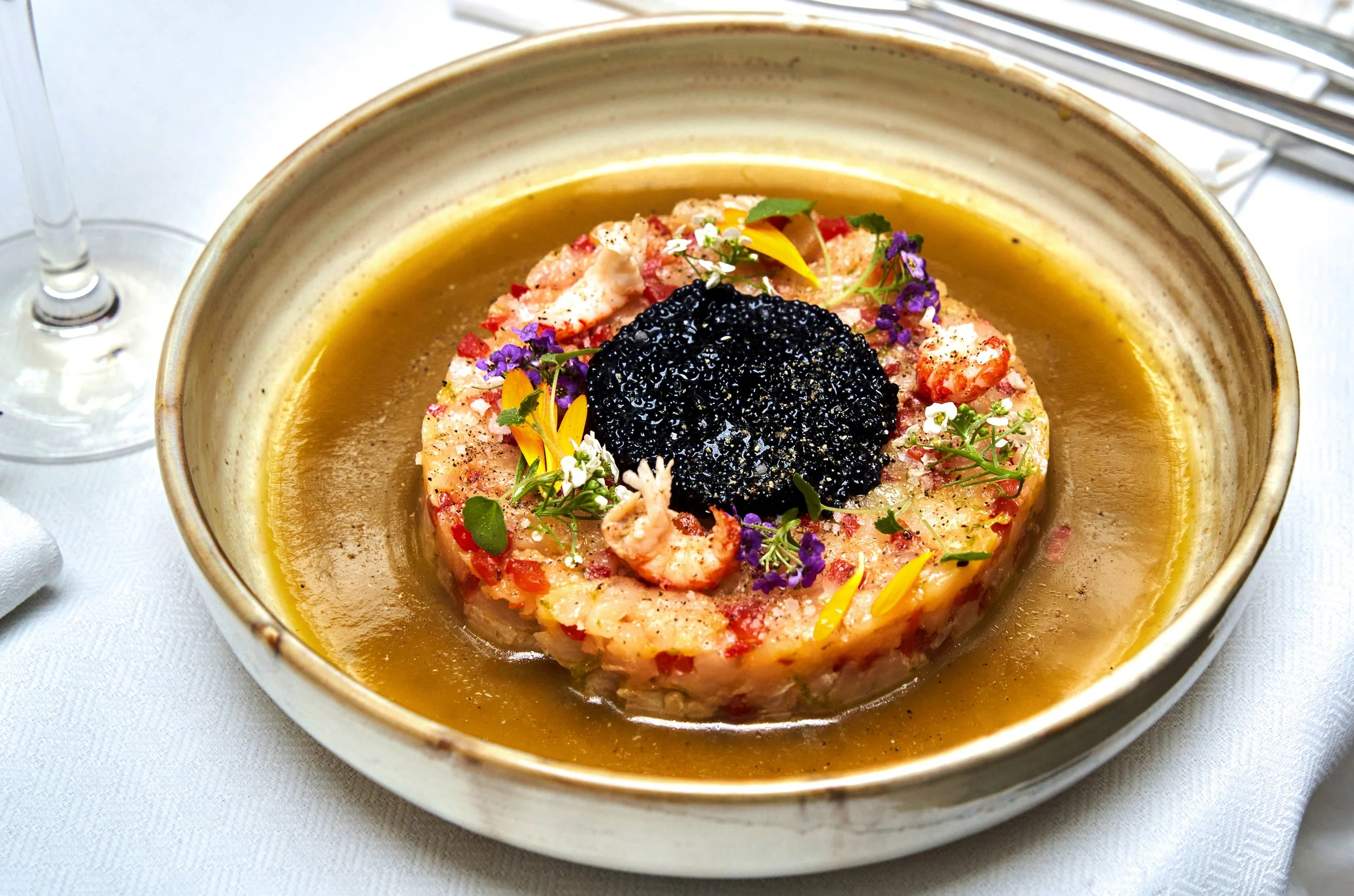 Tartare de poisson garnie de fleurs comestibles et de caviar noir, dans une assiette en céramique