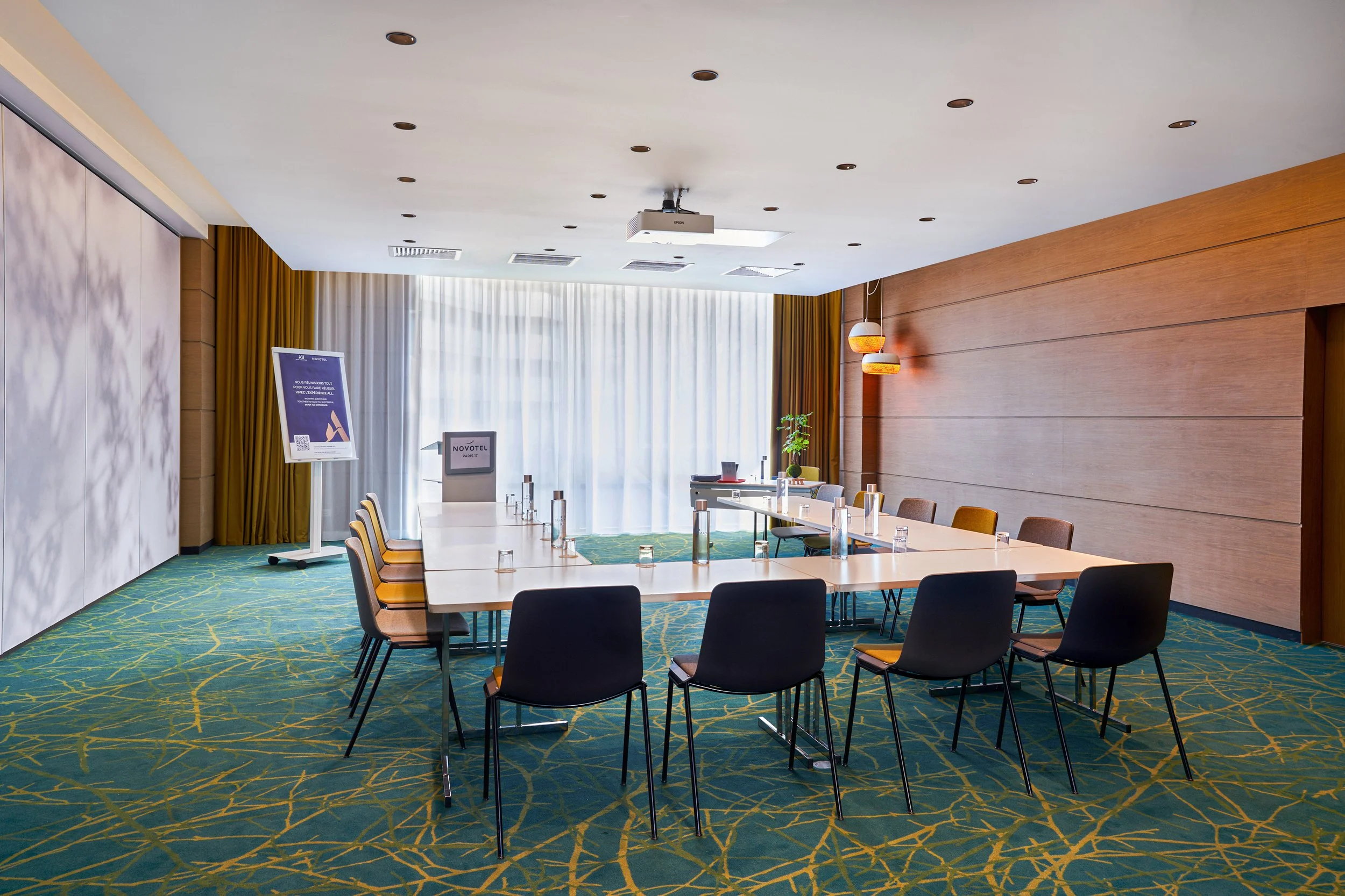 Salle de réunion en U dans un hôtel avec une grande table, chaises, bouteilles d'eau, et décoration moderne.