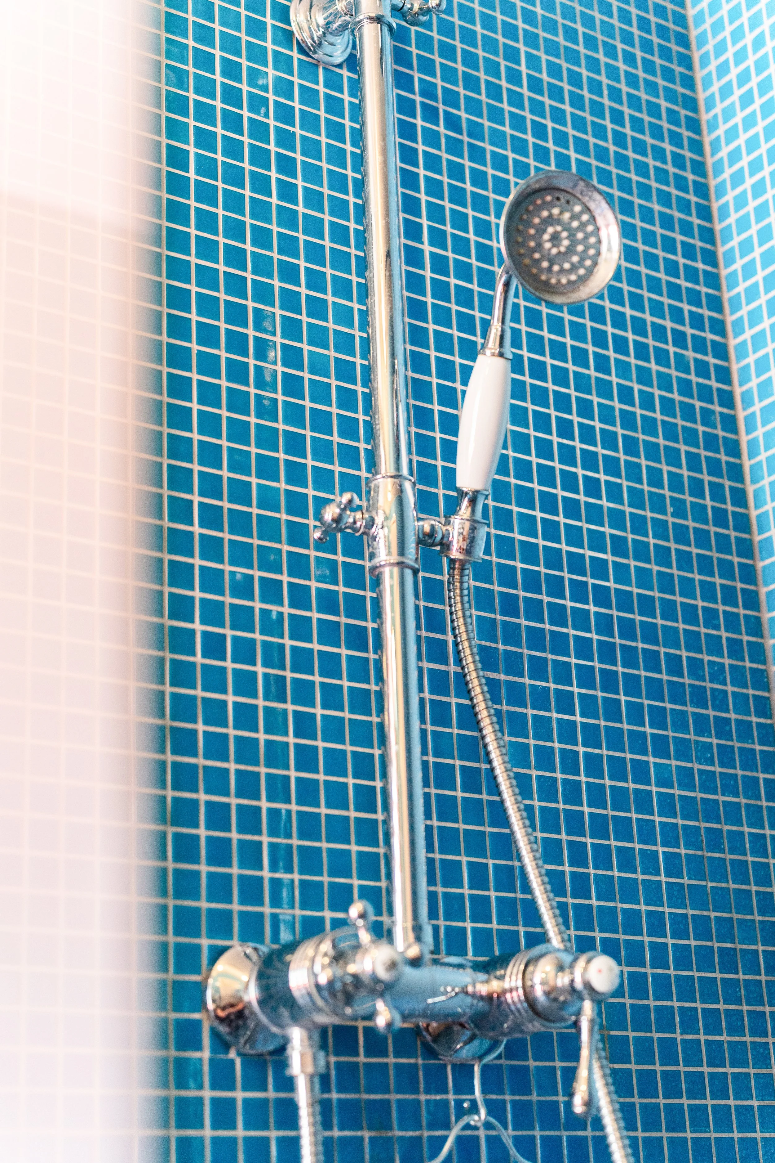 Douchette à main en métal argenté fixée sur un mur recouvert de carreaux bleus dans une douche.