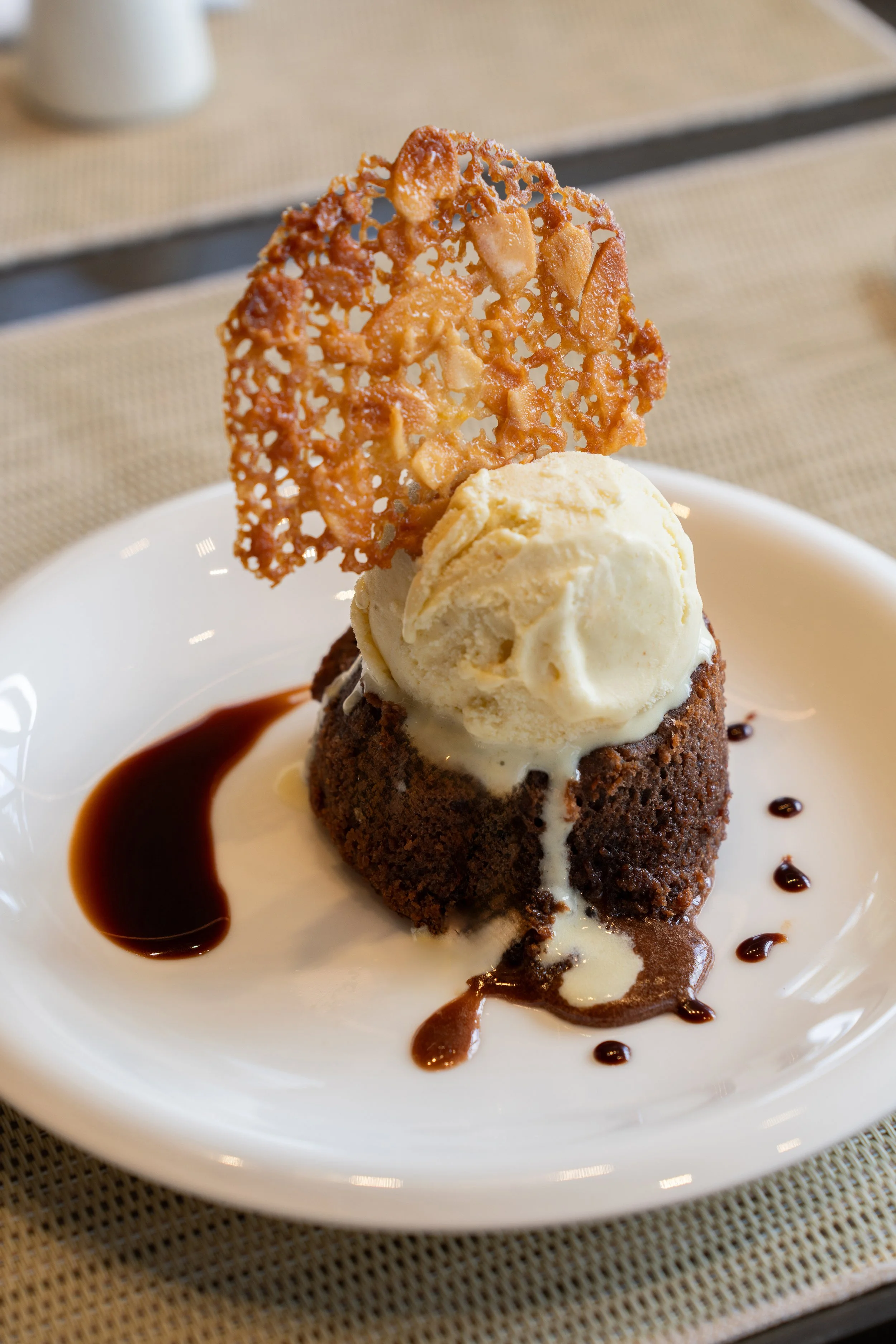 Dessert avec un gâteau au chocolat, une boule de glace à la vanille, une feuille de caramel croustillant, sauce au chocolat et décorations de chocolat.