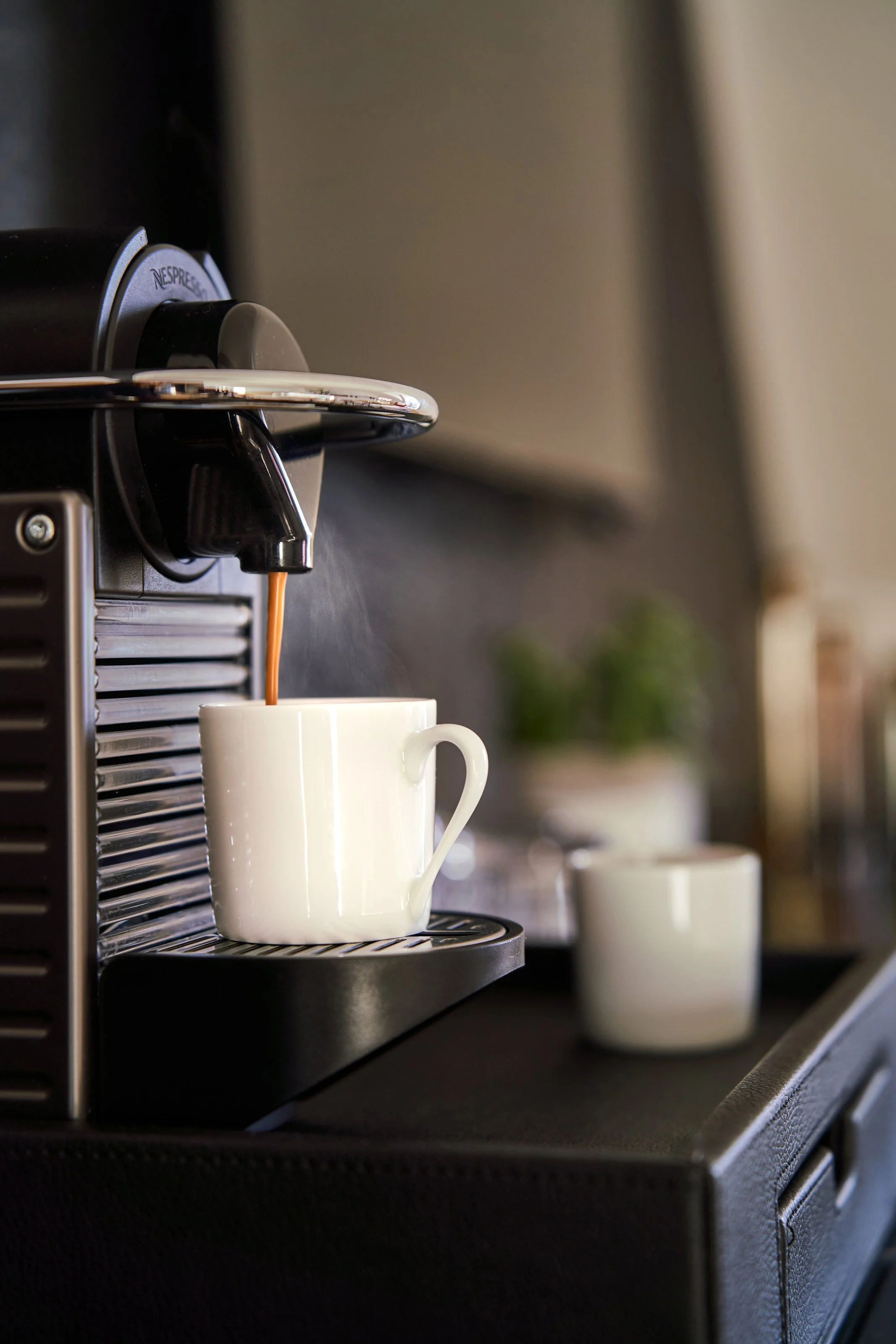 Une machine à café automatique préparant un café dans une tasse blanche sur un buffet noir.