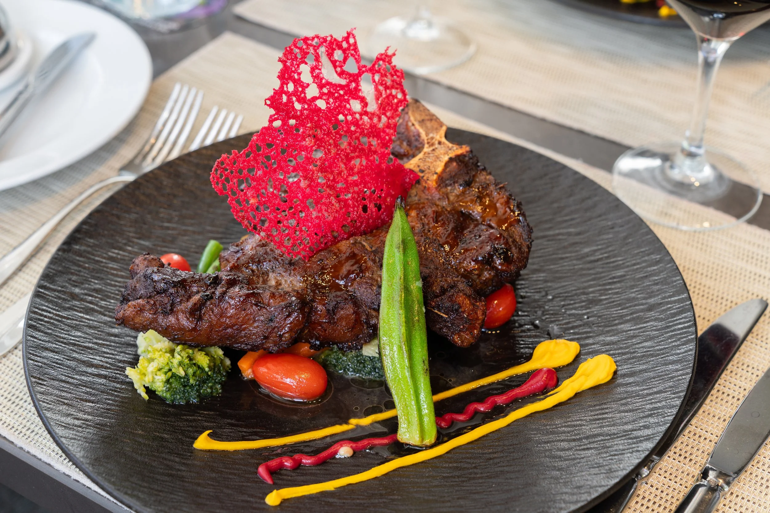 Plat de viande avec légumes, décoration en pâte croustillante rouge, sauces colorées sur une assiette noire