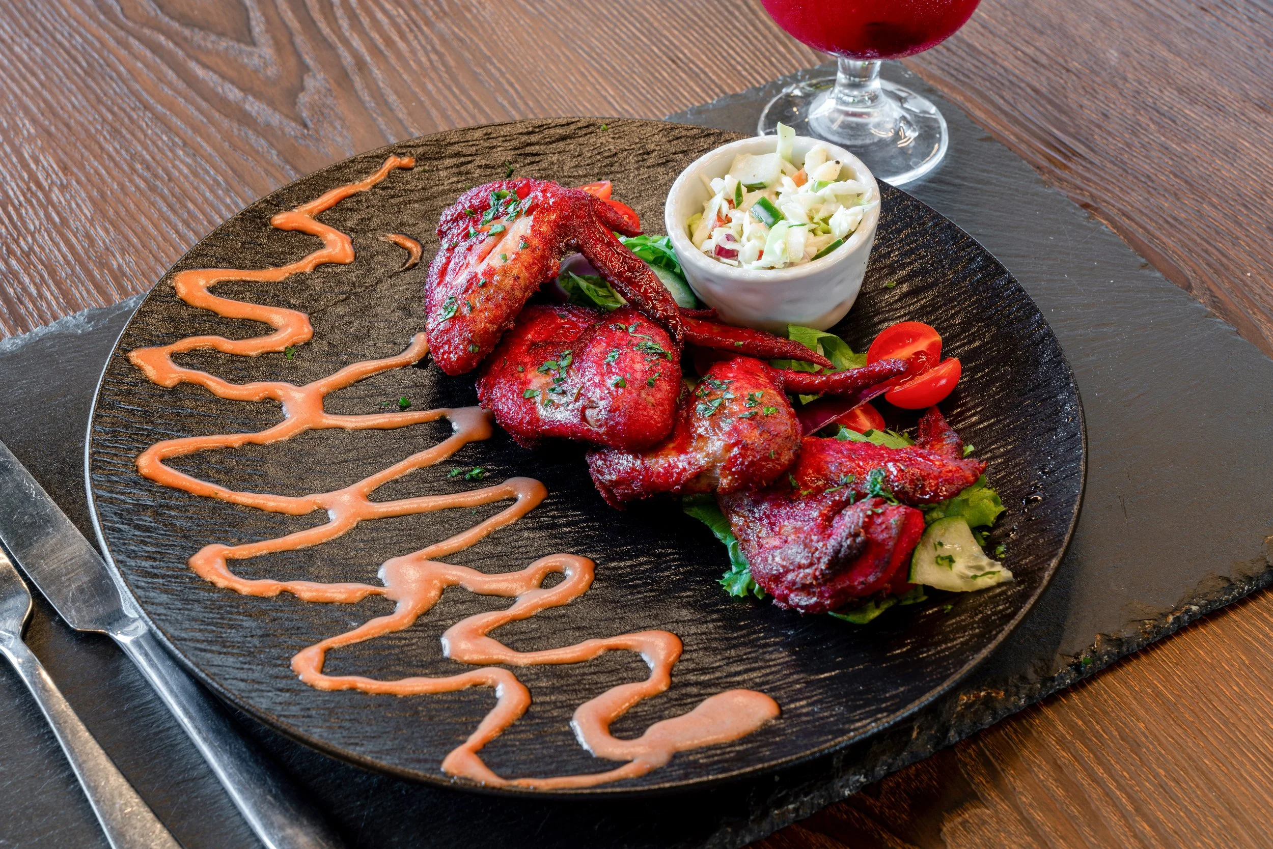 Poisson grillé mariné avec salade et sauce, servi avec une sauce rose décorative sur une assiette noire