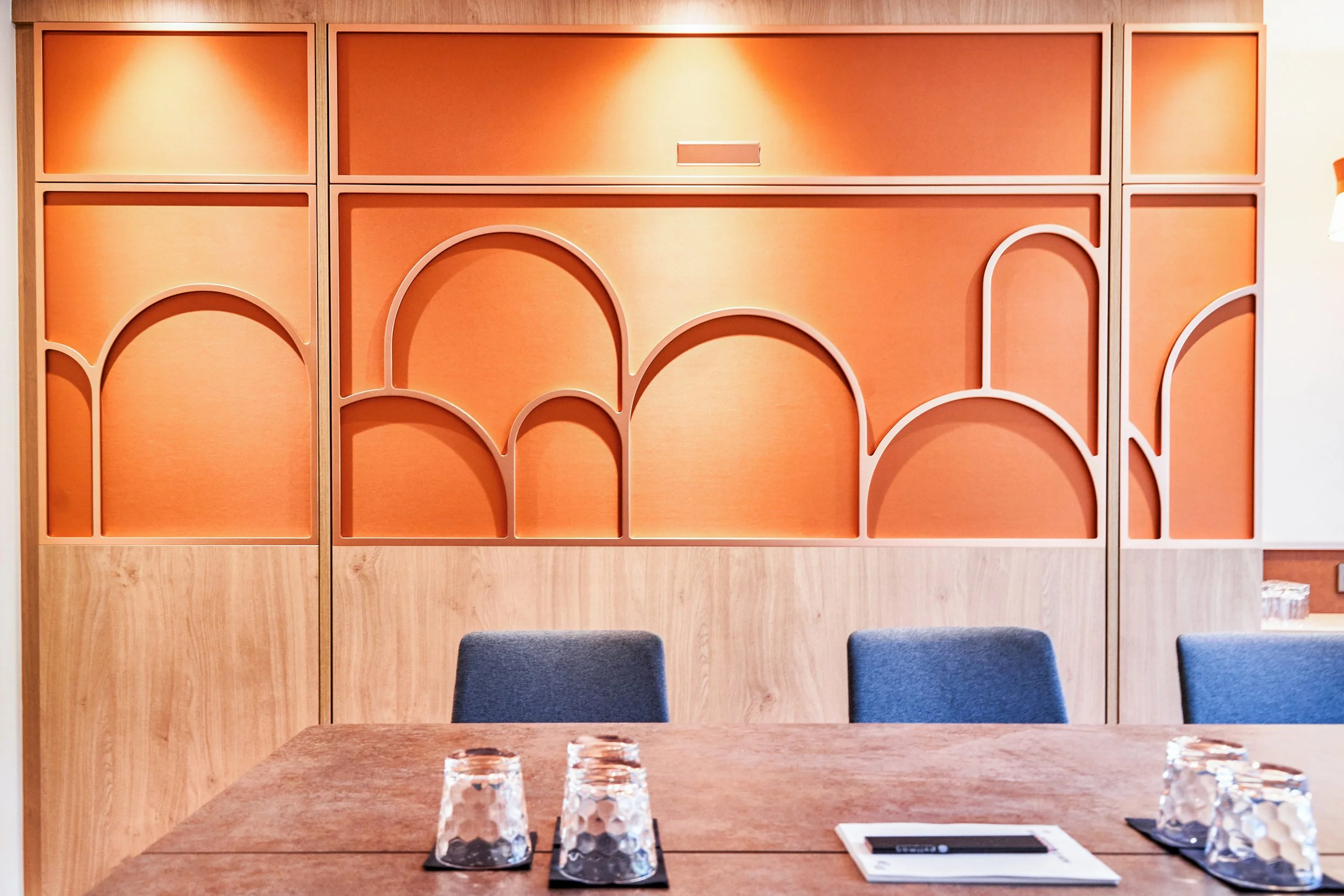 Une cloison en bois orange avec des formes géométriques, et une table en bois avec des verres en verre et un carnet.