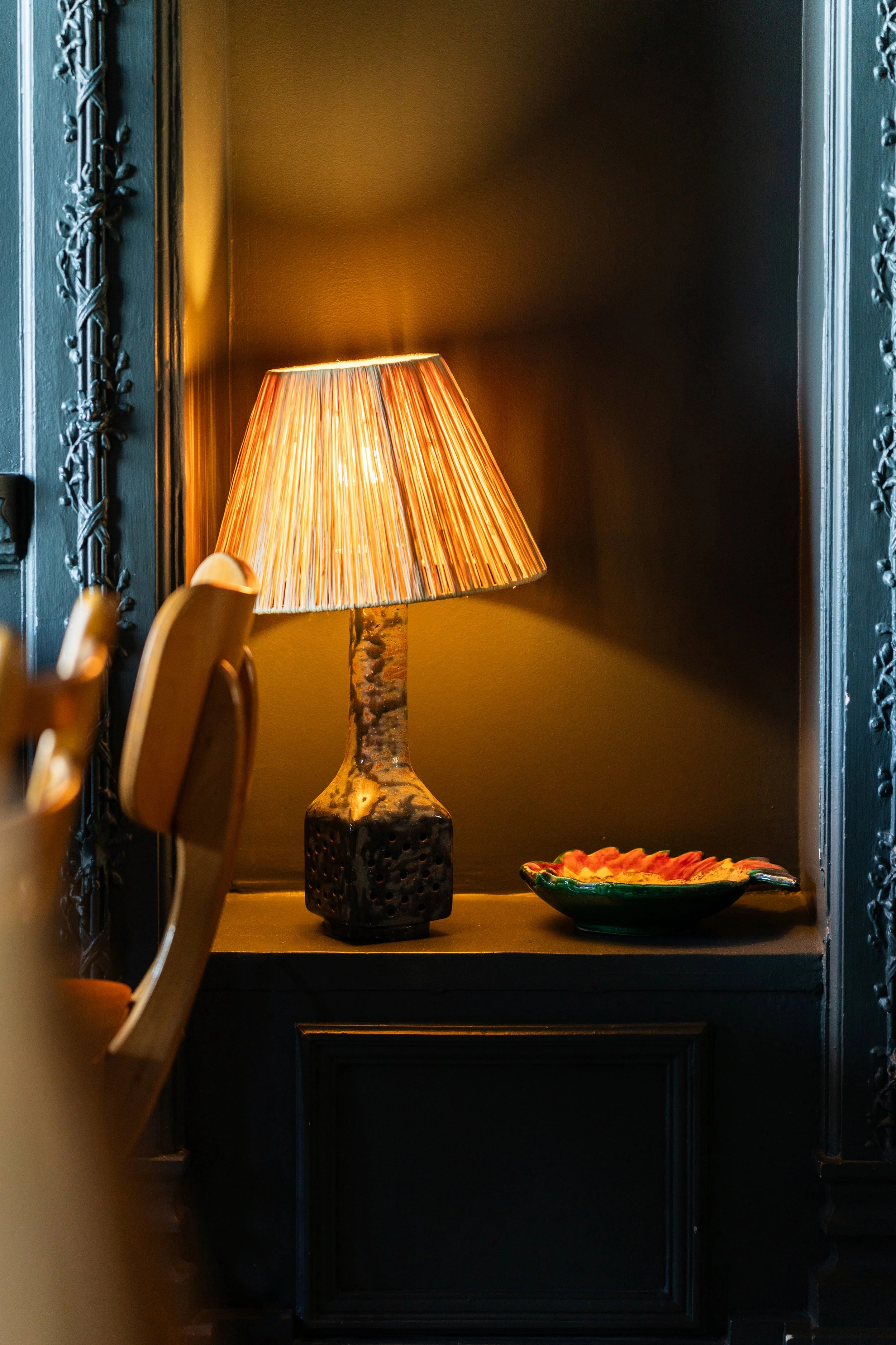 Lampe orange sur une console noire, dans un coin sombre, avec une assiette colorée à côté.