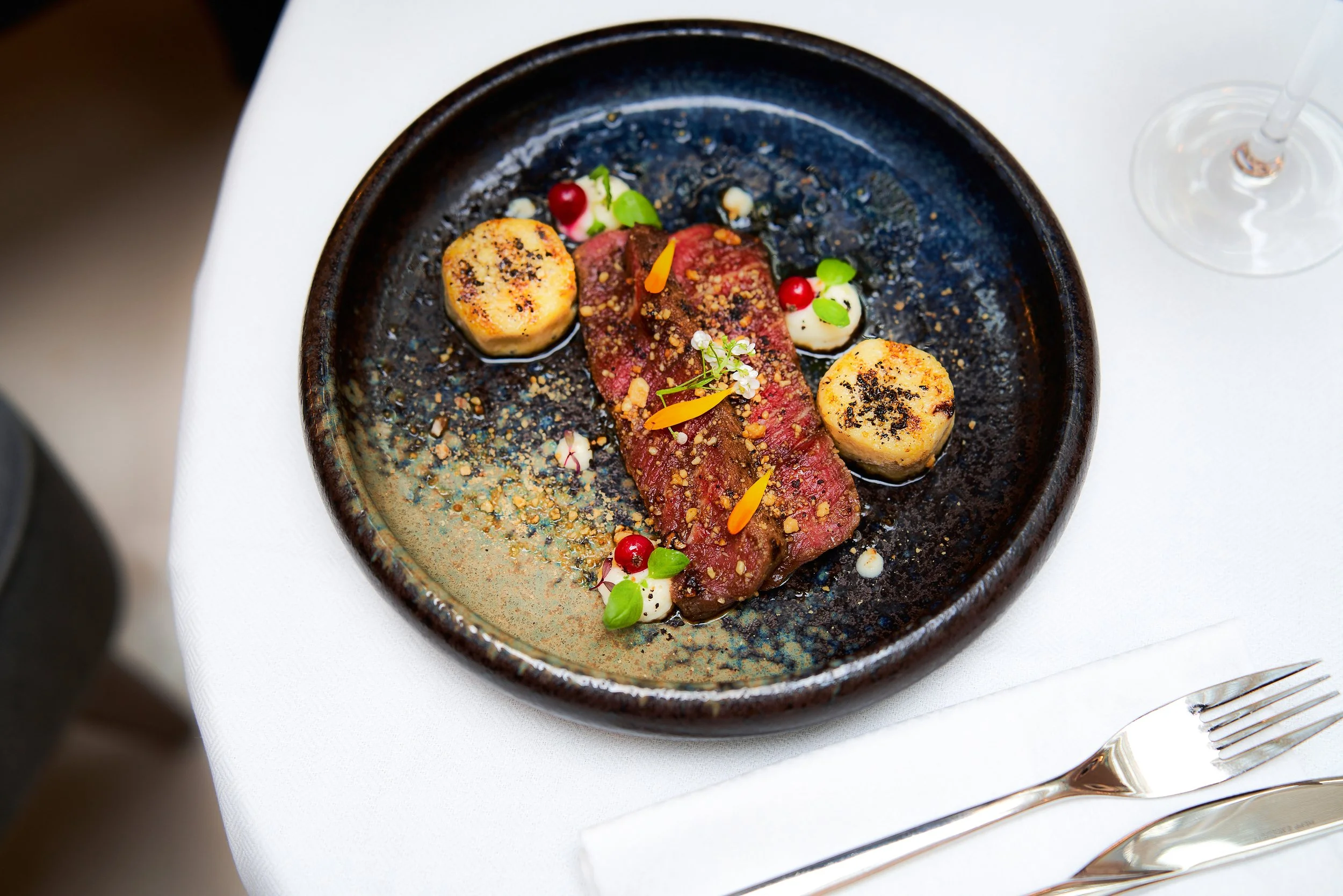 Filet de steak cru, gratin dauphinois, garnitures et décor floral dans une assiette noire