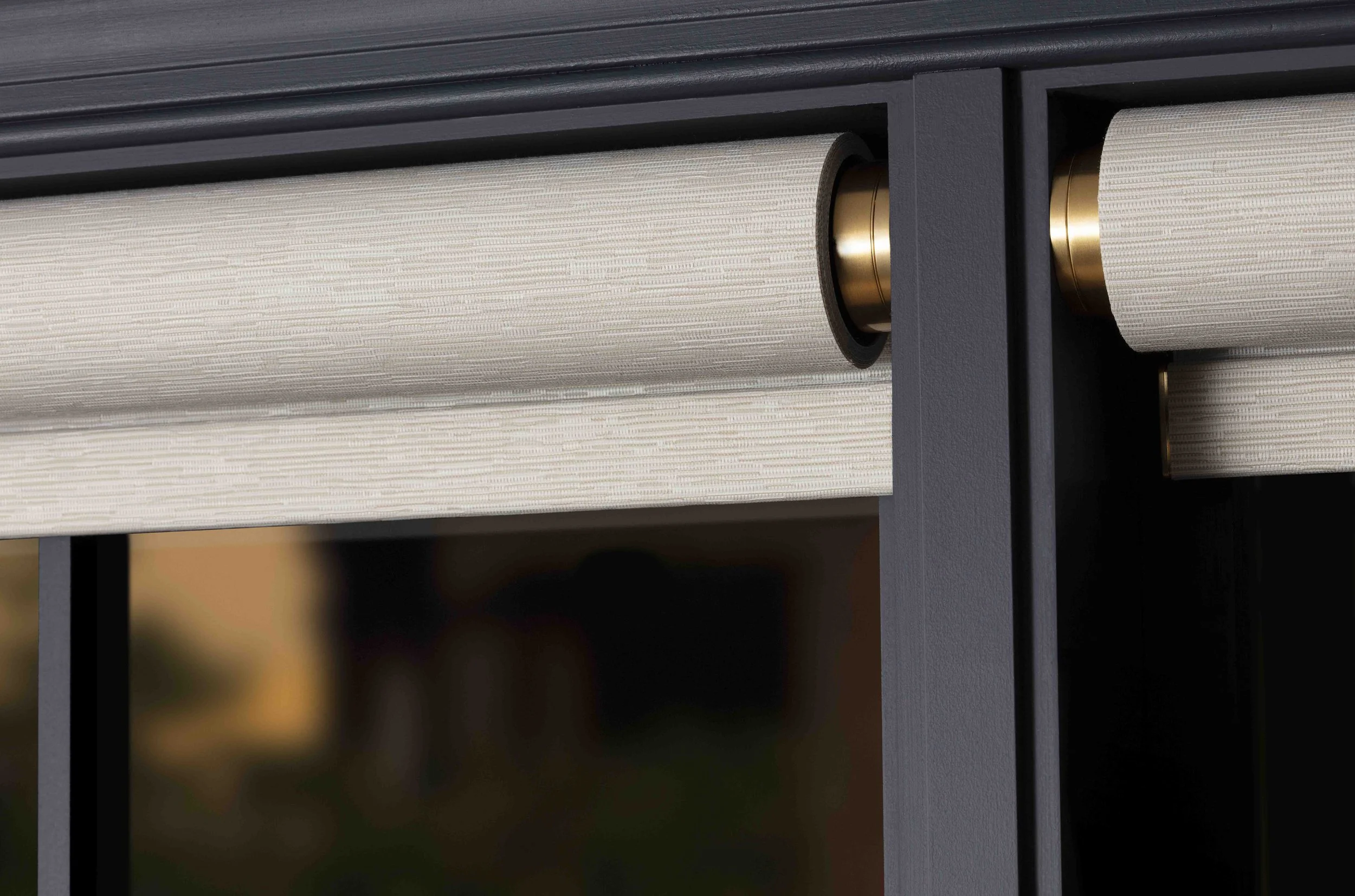 Close-up of a window with a black frame and cream-colored blinds, showing the roller mechanisms inside the frame.