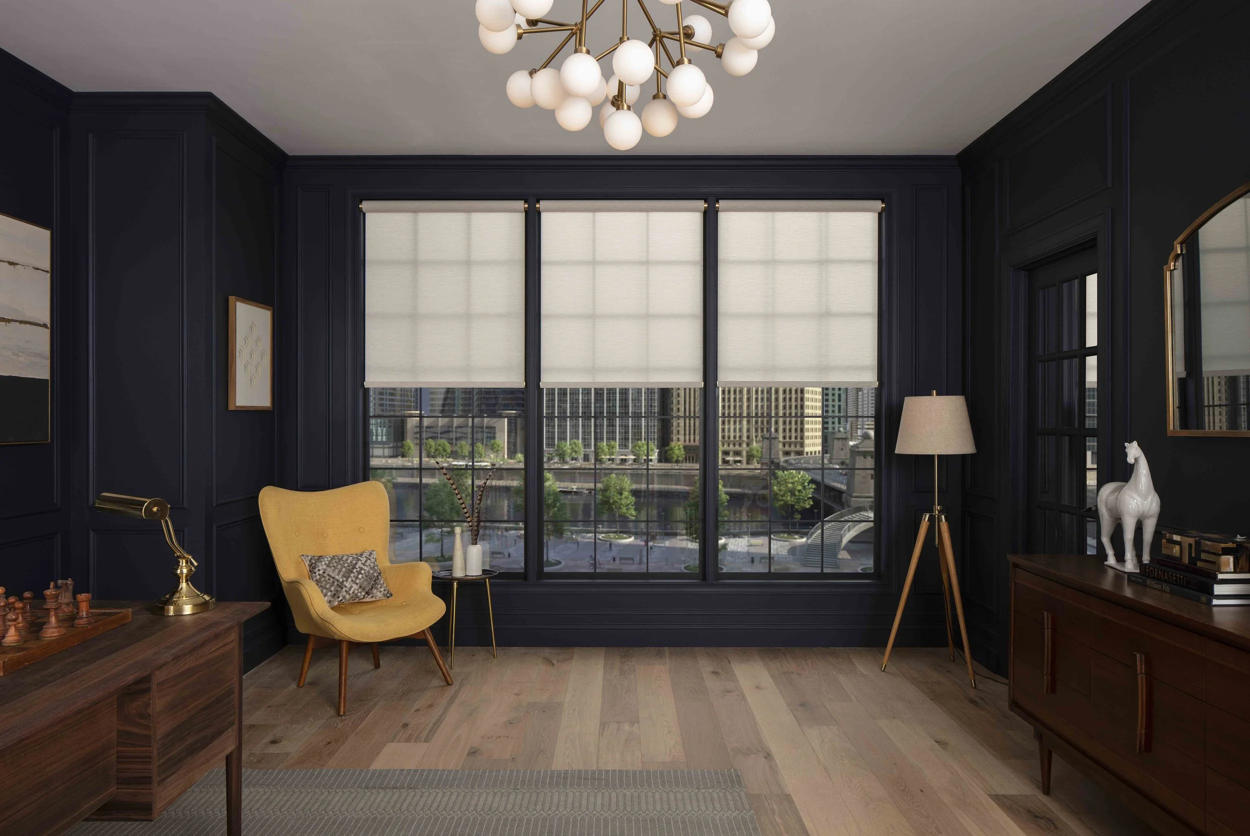 Modern living room with navy blue walls, large windows with shades, wooden furniture, a yellow armchair, a floor lamp, and decorative items including a horse sculpture and framed artwork.
