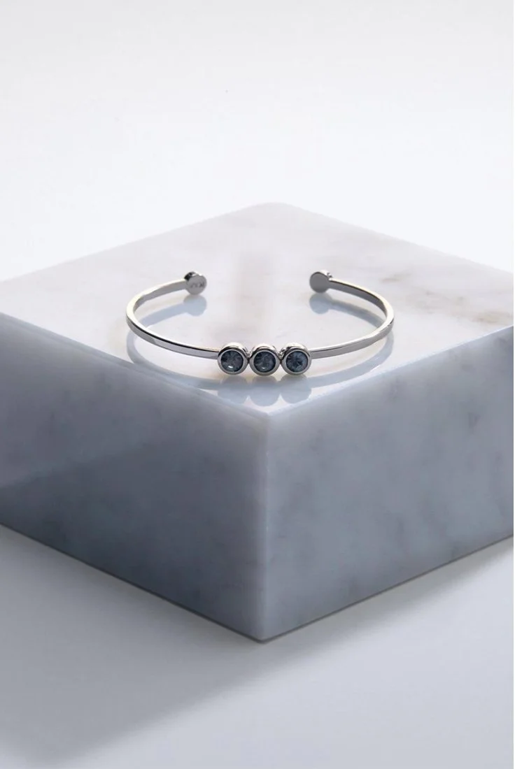 Silver cuff bracelet with three dark gemstones resting on a white marble block.