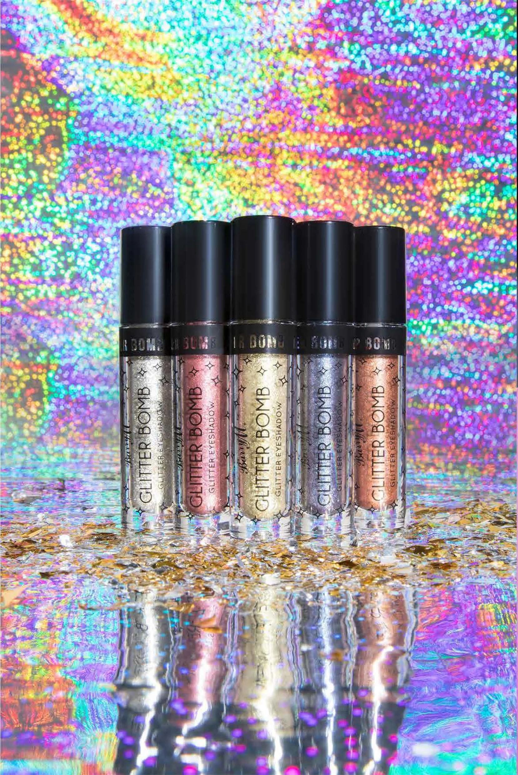 Set of six glitter lip gloss tubes labeled "GLITTER BOMB" and "GLITTER EYESHADOW," standing on a reflective surface with a colorful, holographic background.