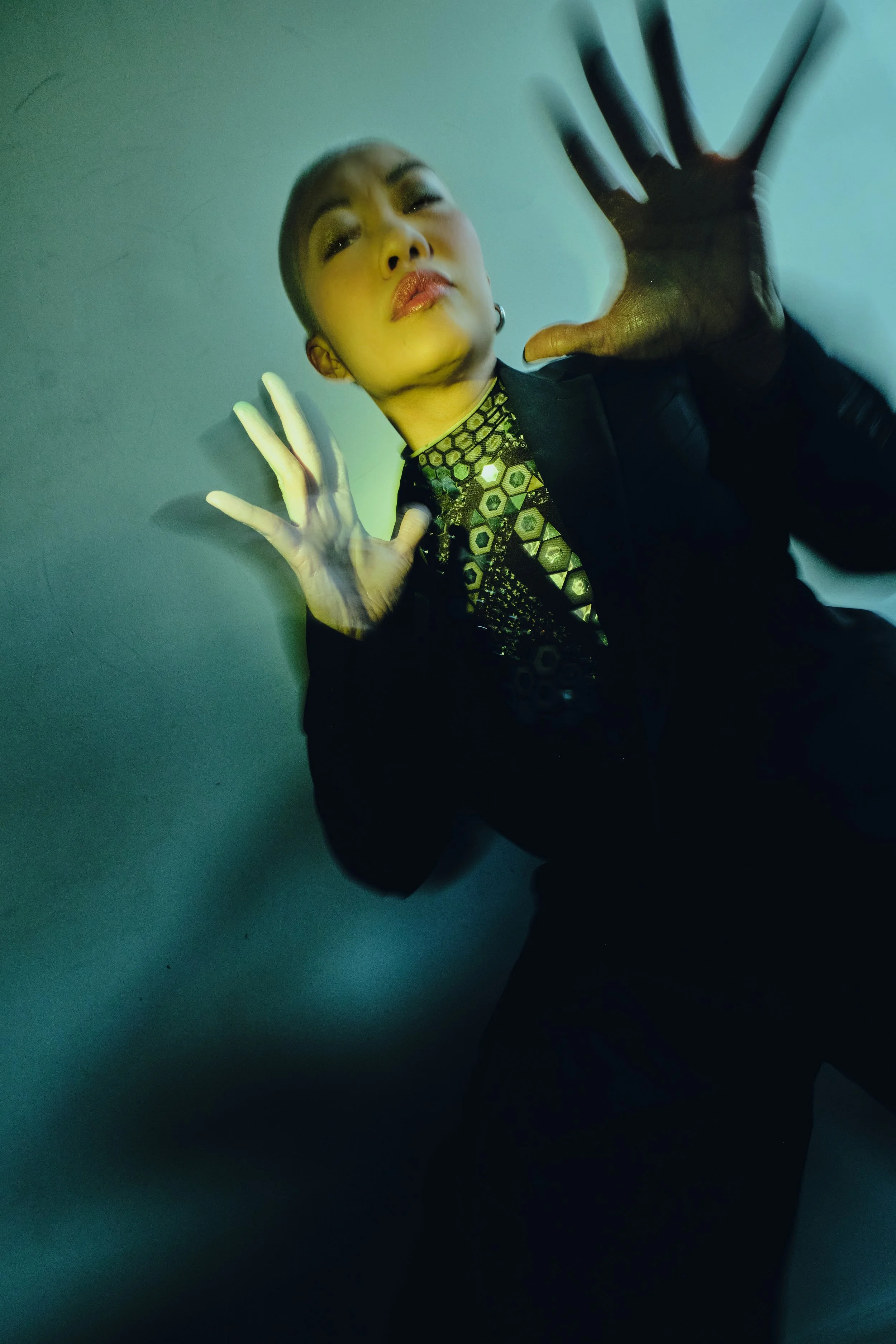 A person with short hair and makeup, wearing a patterned shirt and black jacket, pressing hands against a glass wall with a serious expression. JSnaps Photography New York City Fashion lifestyle photography 