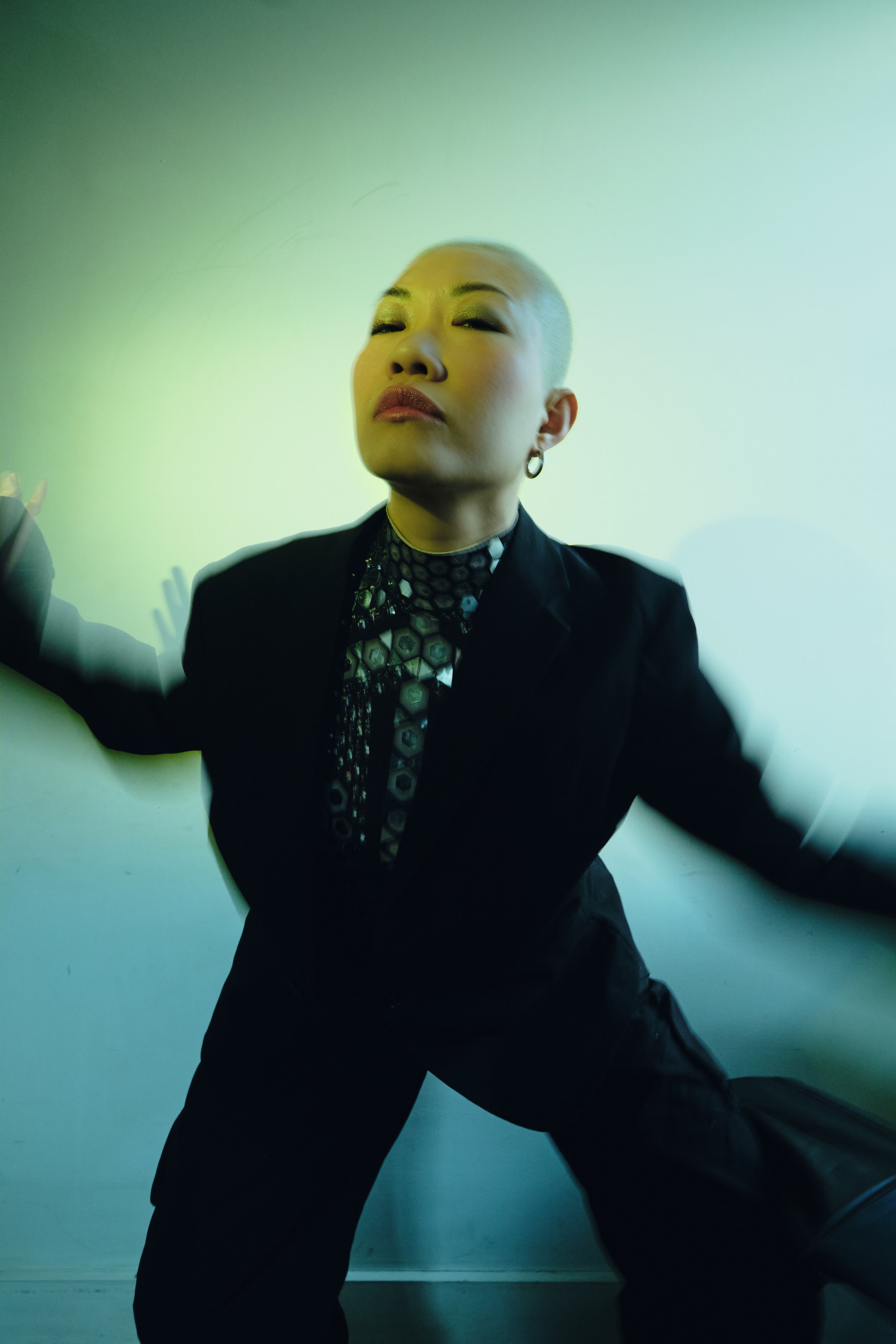 A person with a short platinum blonde hairstyle, wearing a black blazer and patterned shirt, posing confidently against a plain wall. JSnaps Photography New York City Fashion lifestyle photography 