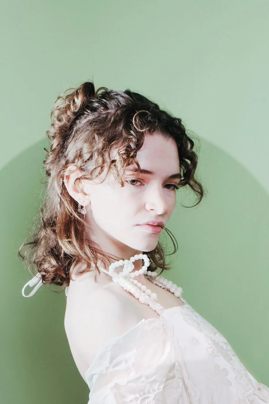 A young woman with curly hair, wearing pearl jewelry and a light-colored floral dress, against a green background. Headshot of a female JSnaps Photography New York City Fashion lifestyle photography 