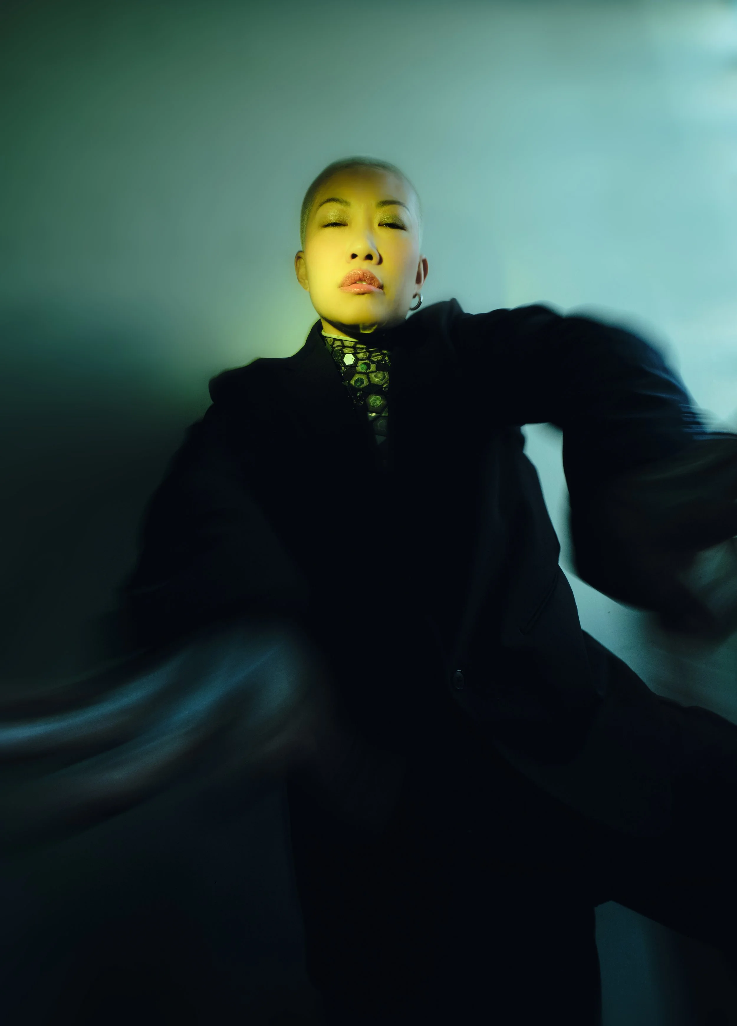 A person with short hair and hoop earrings wearing a dark jacket and patterned top, taking a selfie with a confident expression against a plain background. JSnaps Photography New York City Fashion lifestyle photography 