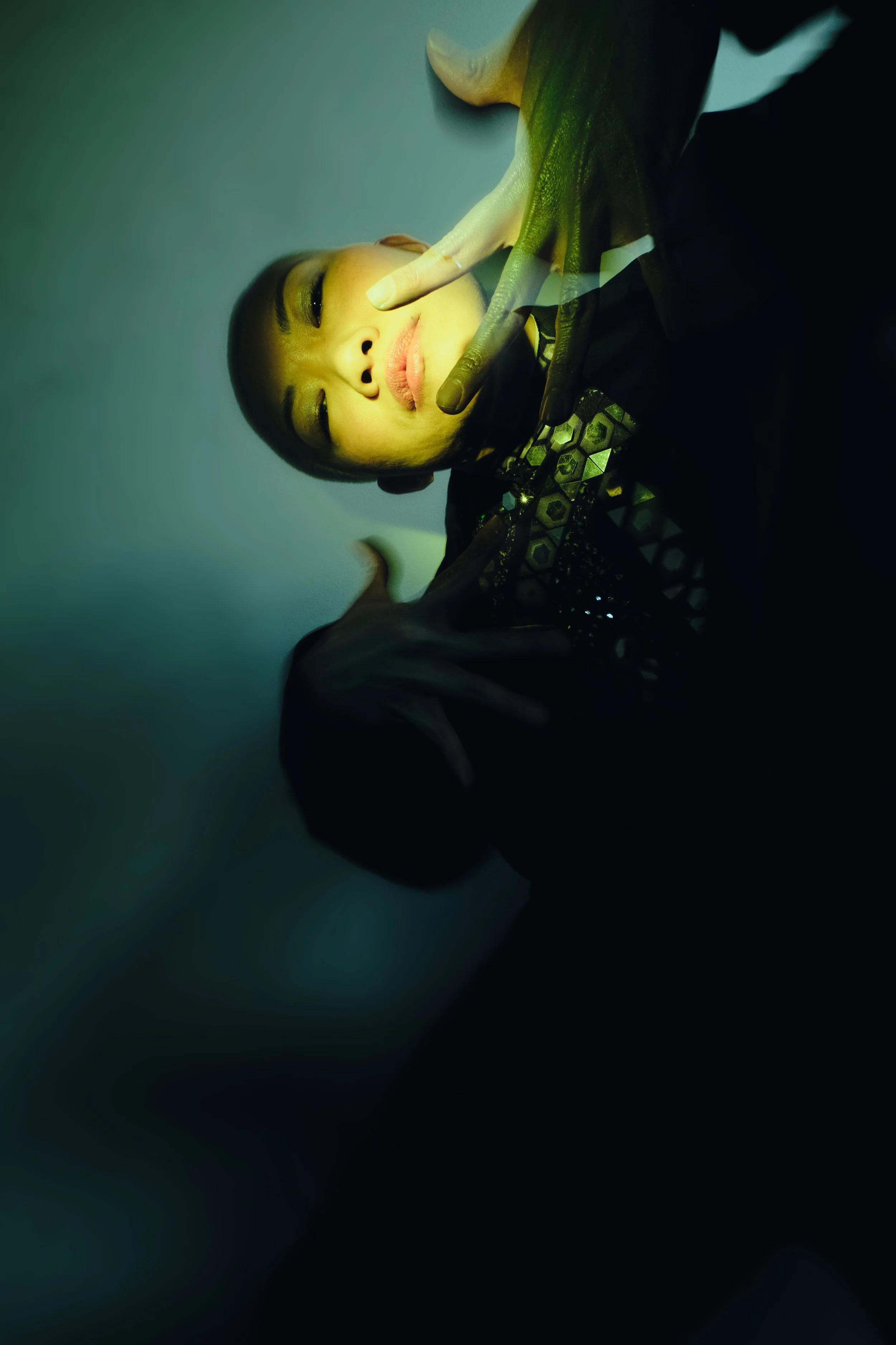 A young woman with makeup and dark clothing posing with her eyes closed, making peace signs near her face. She is illuminated by a greenish-yellow light. JSnaps Photography New York City Fashion lifestyle photography 