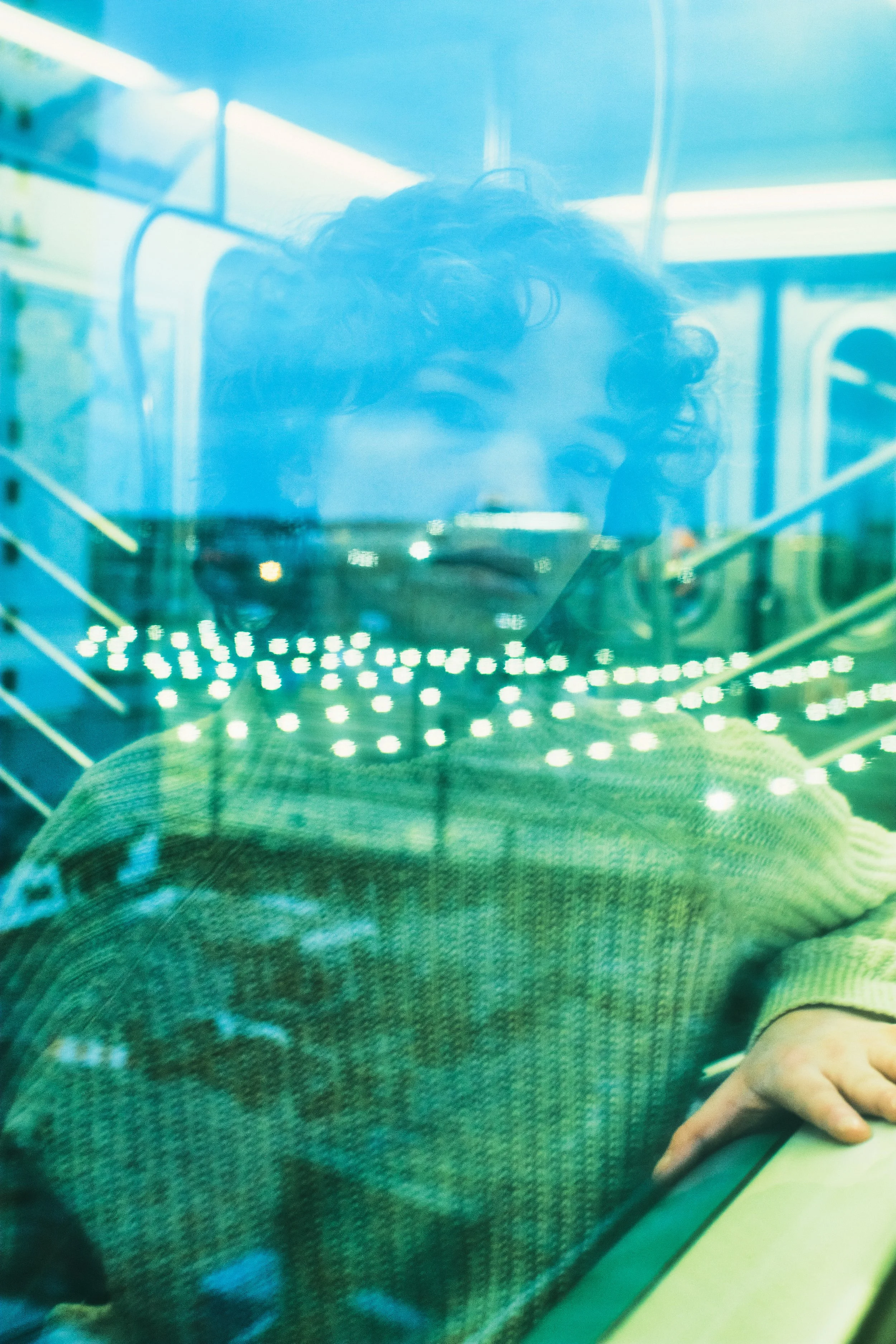 A woman with curly hair taking a selfie through a glass window, with city lights reflected on the glass and their hand resting on a surface. JSnaps Photography New York City Fashion lifestyle photography 