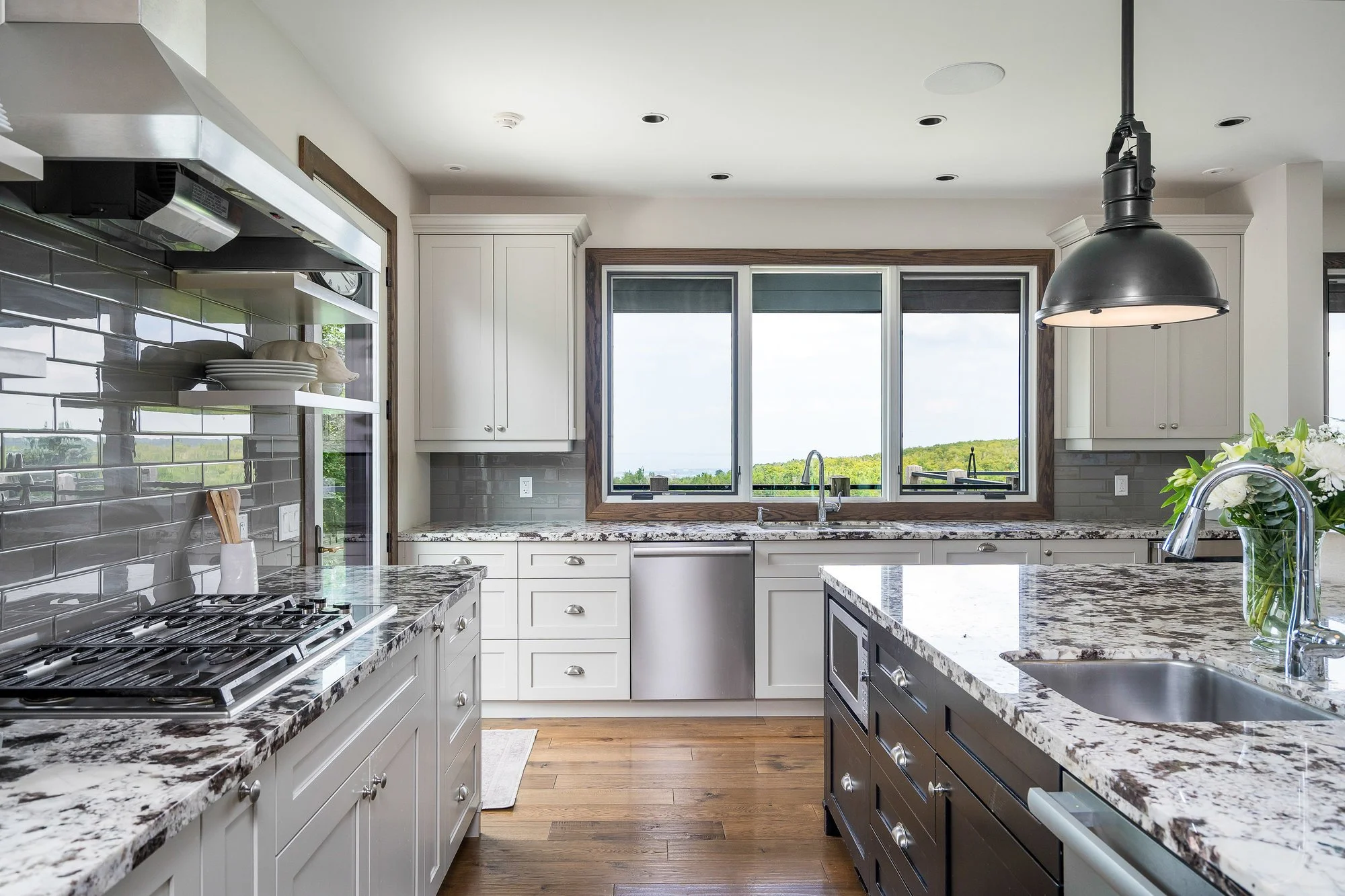 Modern kitchen with white cabinets, granite countertops, gray subway tile backsplash, and a large window overlooking green landscape.
