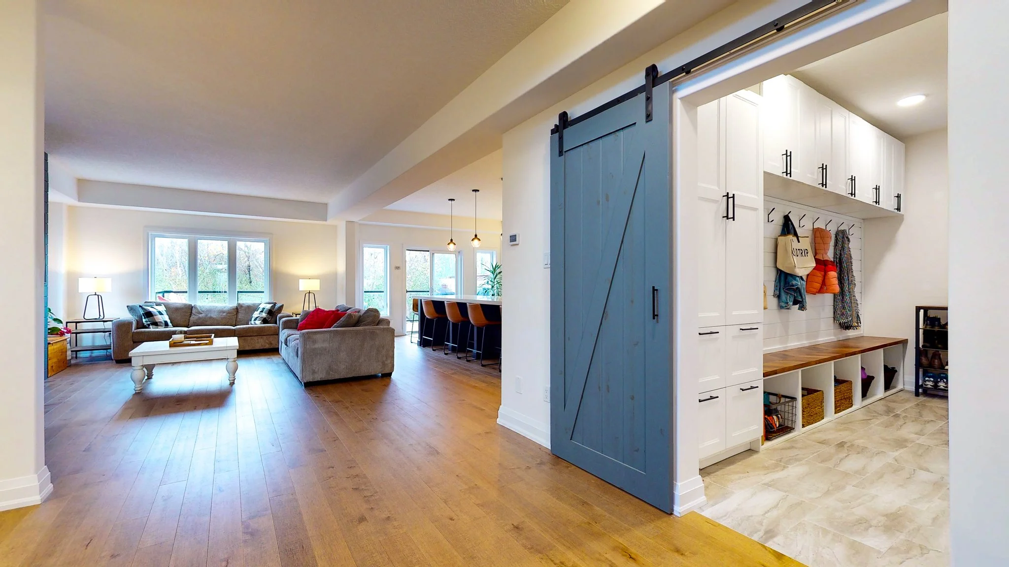 Open-concept living room and mudroom with hardwood floors, beige sofas, and a sliding barn door.