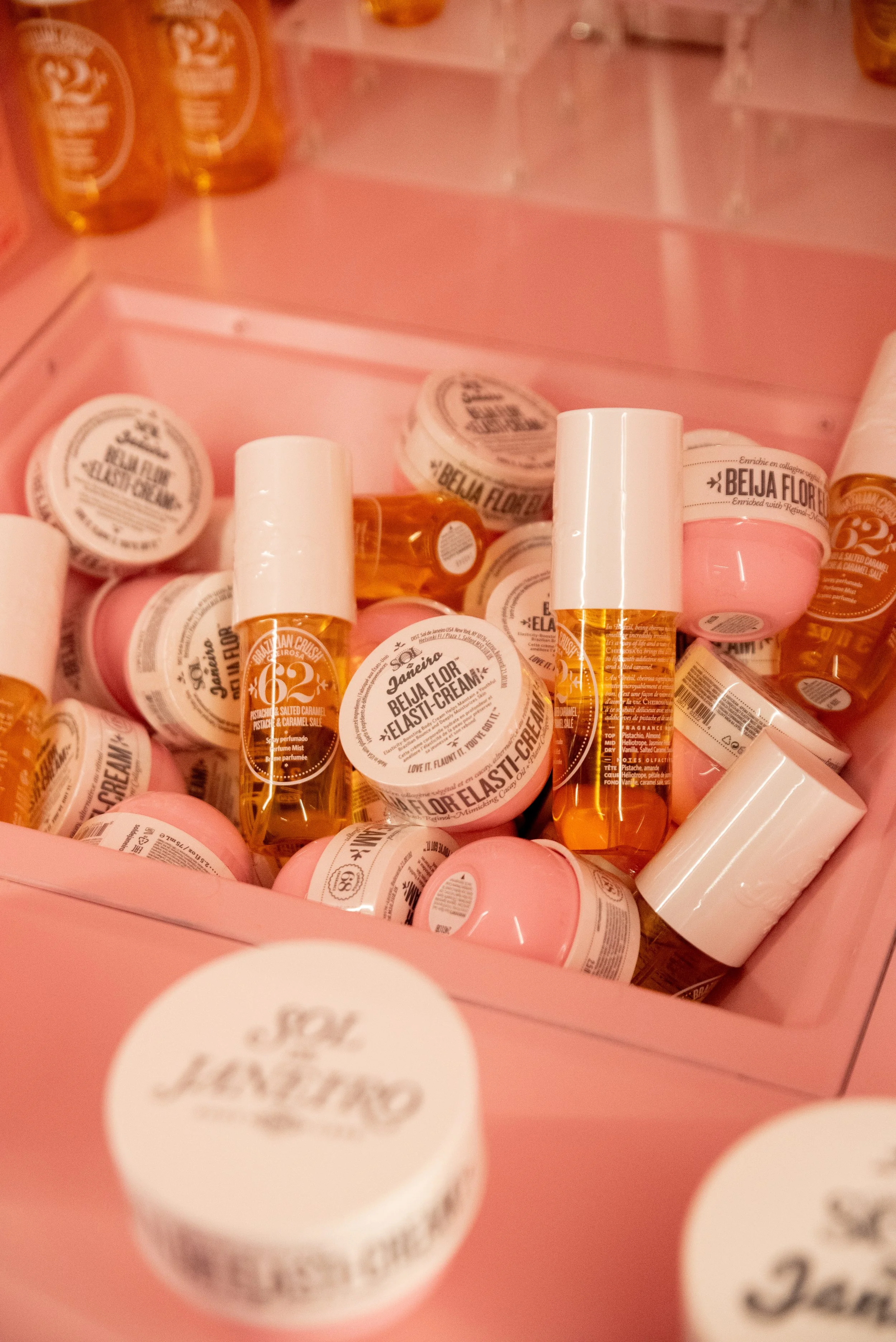 A collection of pink and white containers with labels displaying the product name 'Beija Flor Elastif-Cream' and small amber bottles arranged in a pink box.