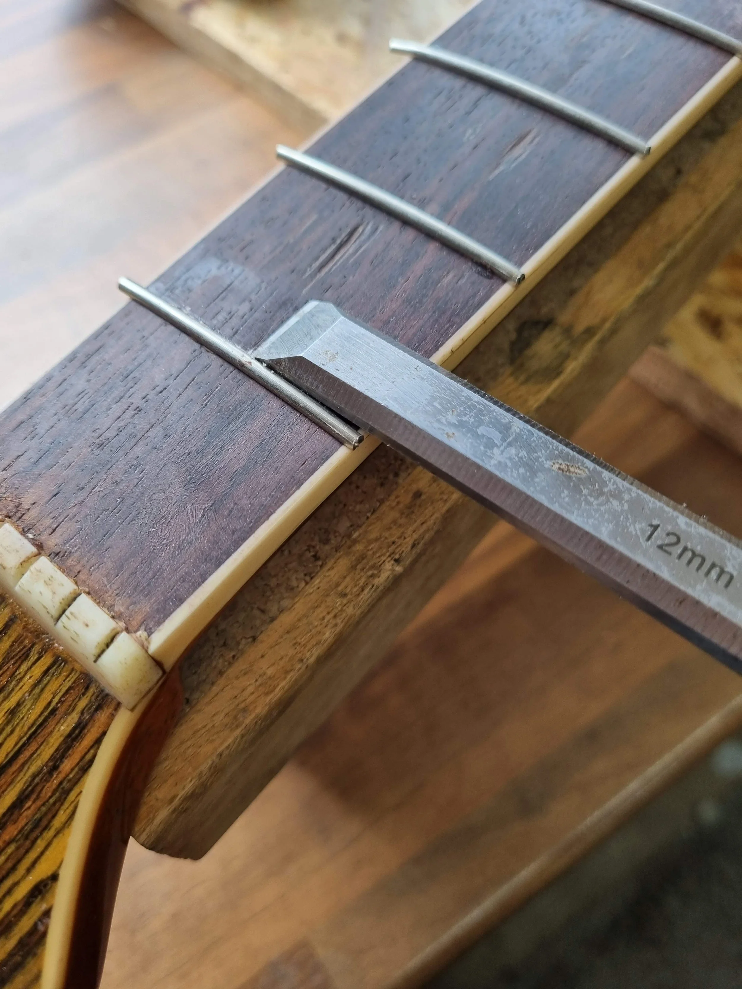 Close-up of a guitar neck and chisel removing glue after fretting.