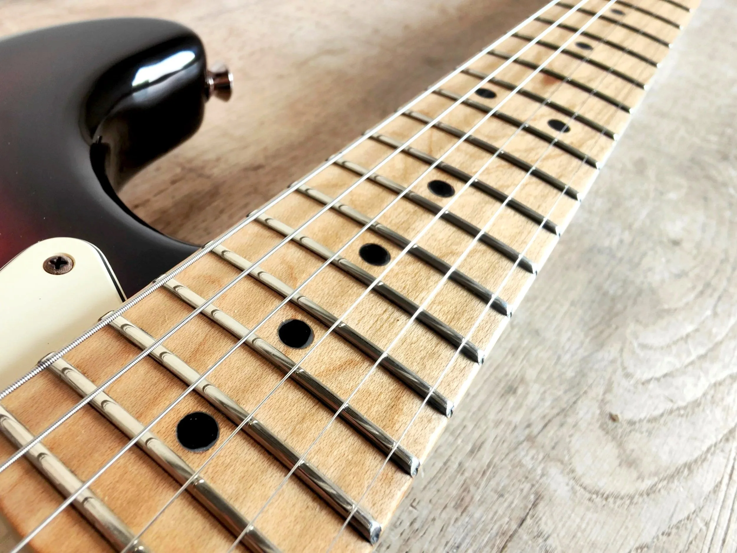 Close-up of a sunburst electric guitar's fretboard and strings, resting on a wooden surface.
