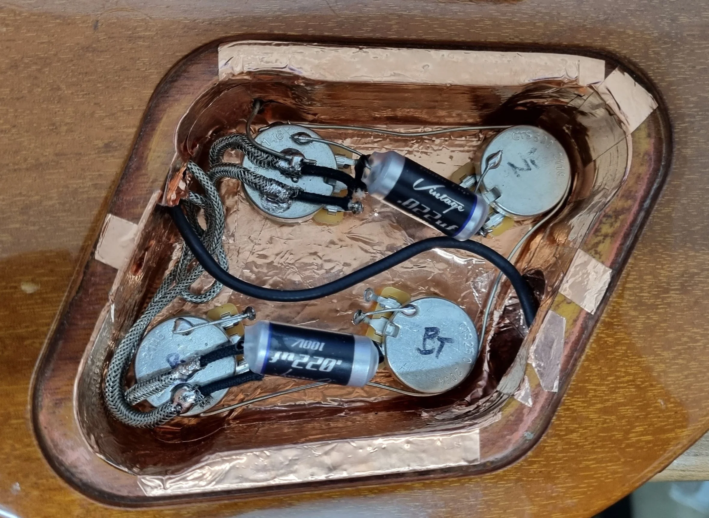 Electronics inside a LEs Paul style guitar with capacitors, wiring, and a copper reflective interior.