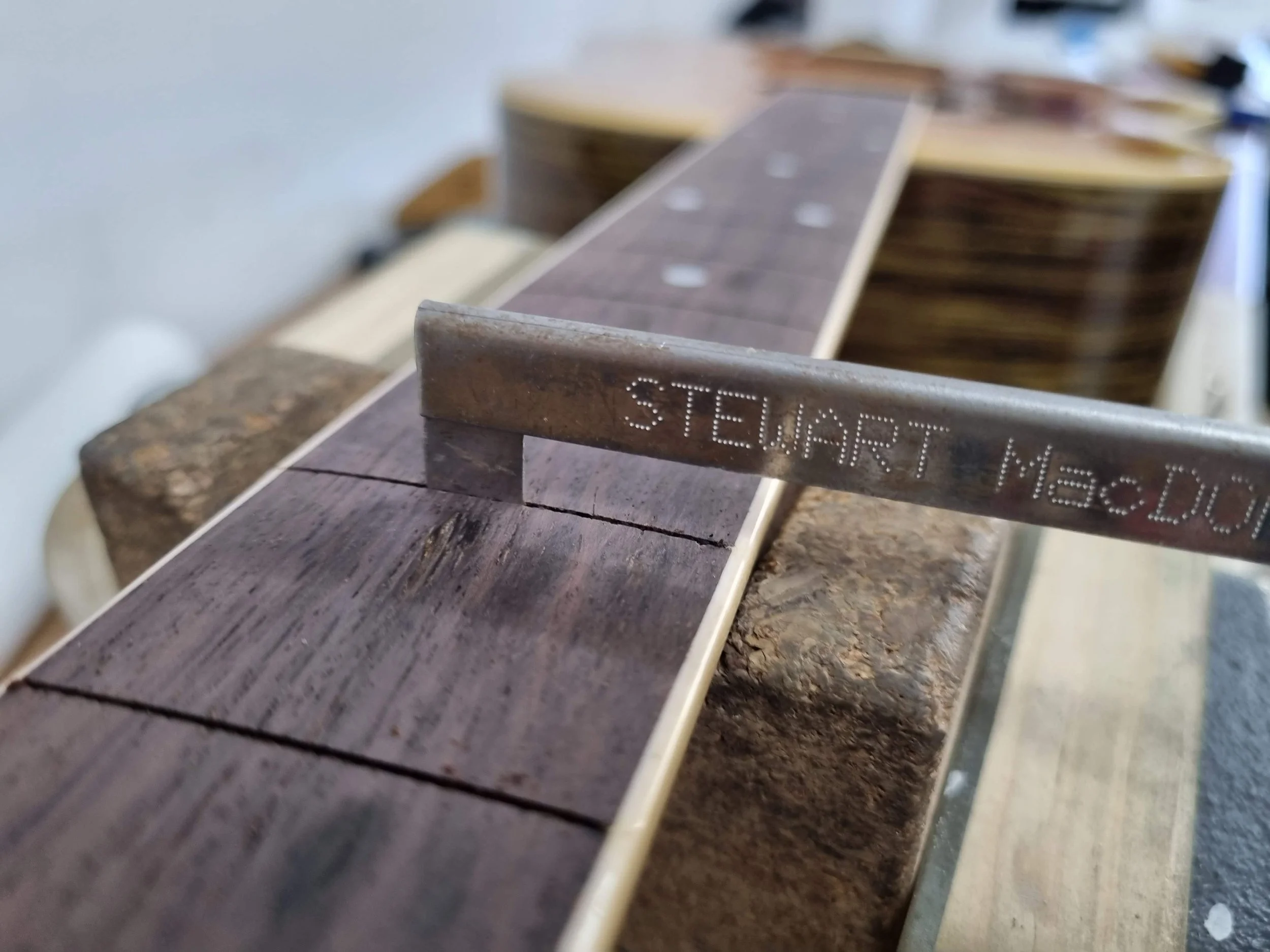 Close-up of a guitar neck and fretboard under construction or repair, with a fret slot saw