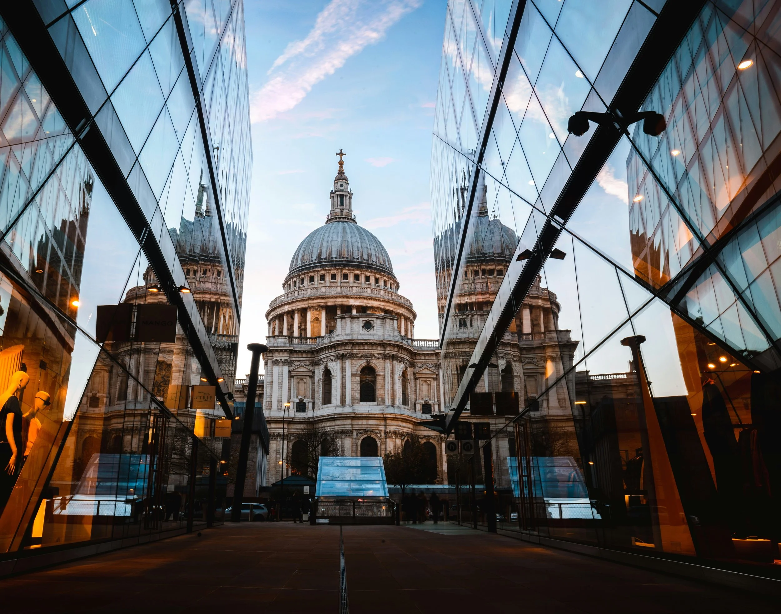 Photo of St. Paul's Cathedral in London, seen through modern glass buildings reflecting the sky and the cathedral.