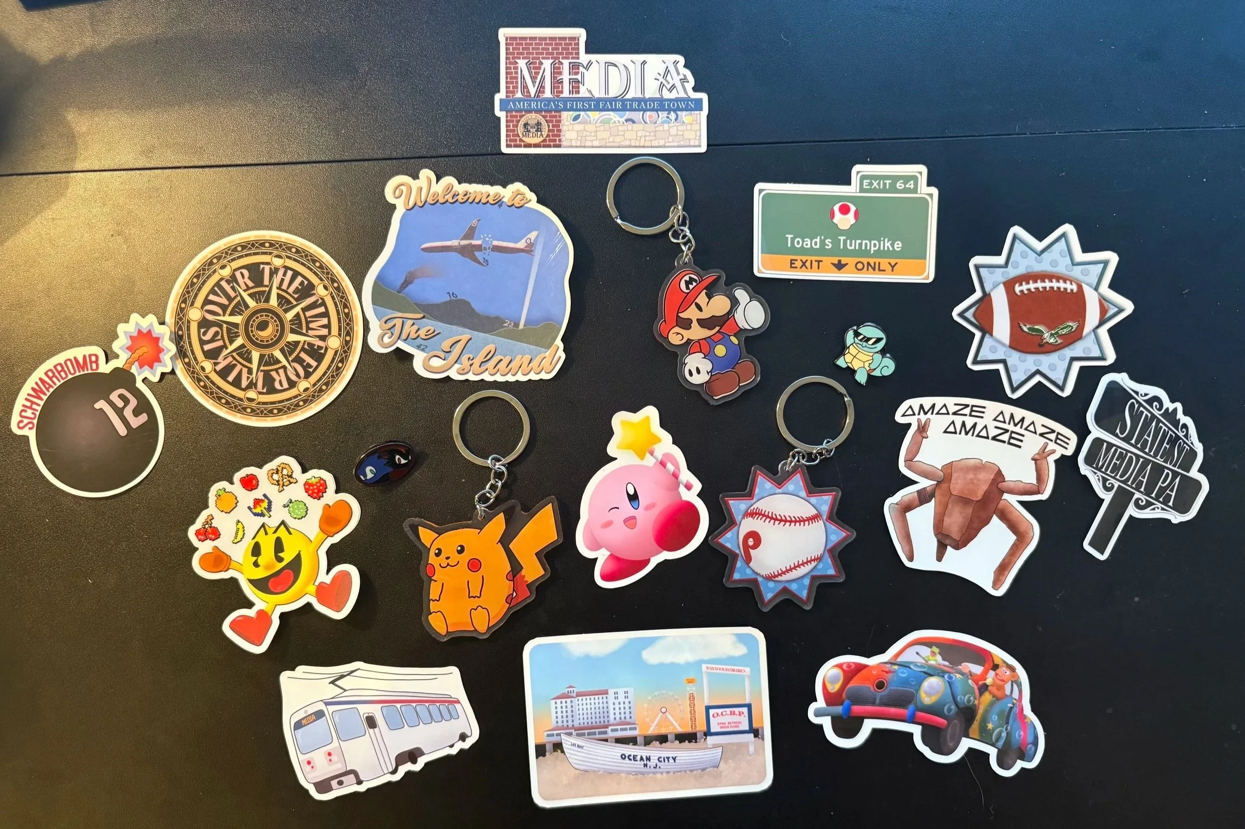 A small selection of some of my designs as stickers, keychains and pins, ranging from Media, PA designs, to Nintendo games, to TV shows like The Traitors and LOST and some Phillies/Eagles designs.