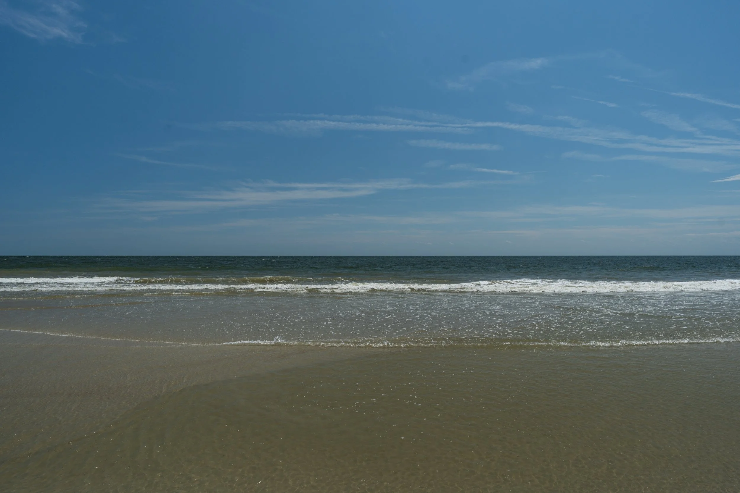 A serene beach with gentle waves hitting the sandy shore under a blue sky with a few clouds.