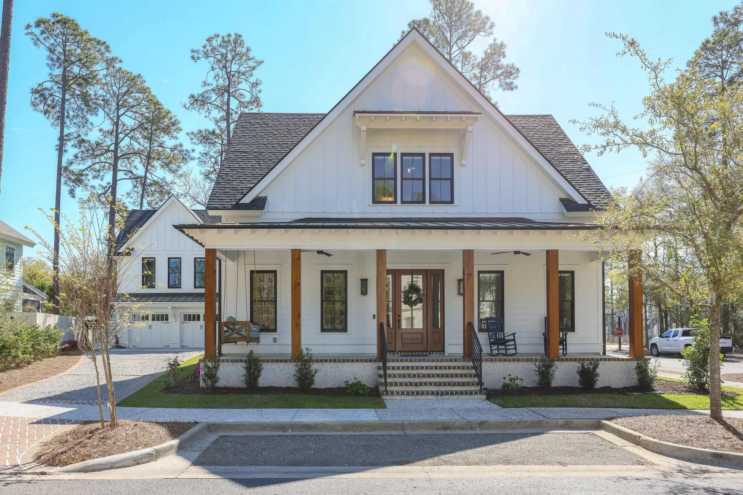 A modern white house with a front porch, set against a sunny sky with trees in the background.