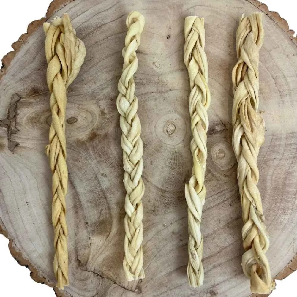 Four premium air-dried braided lamb skin dog chews arranged flat on a rustic wood background.
