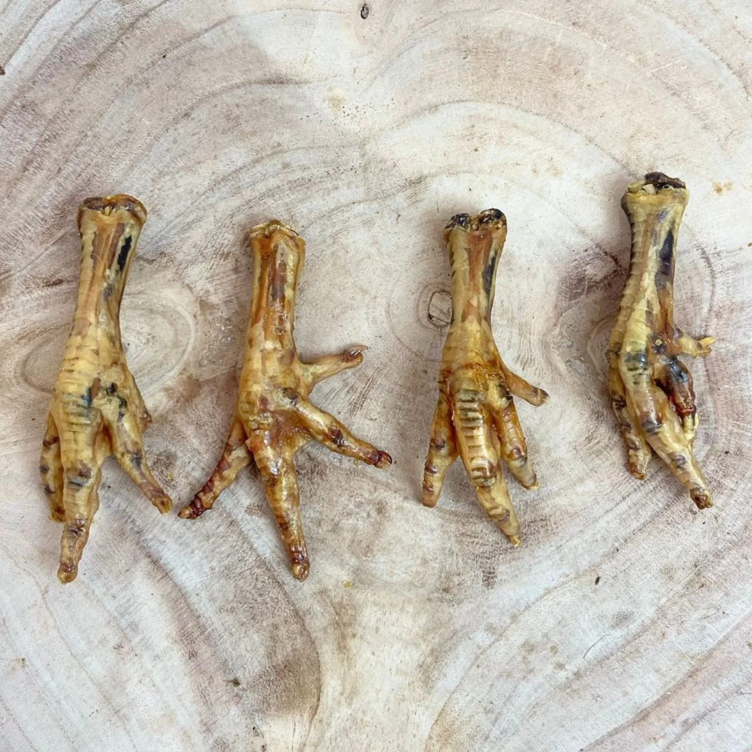 Four Paddock Farm dried chicken feet dog chews arranged side by side on a light-coloured wooden background