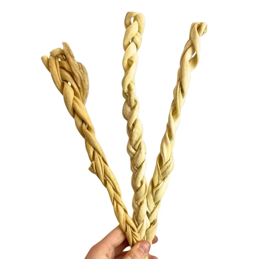 A person holding three 30cm Paddock Farm braided lamb skin dog treats to show texture and size.