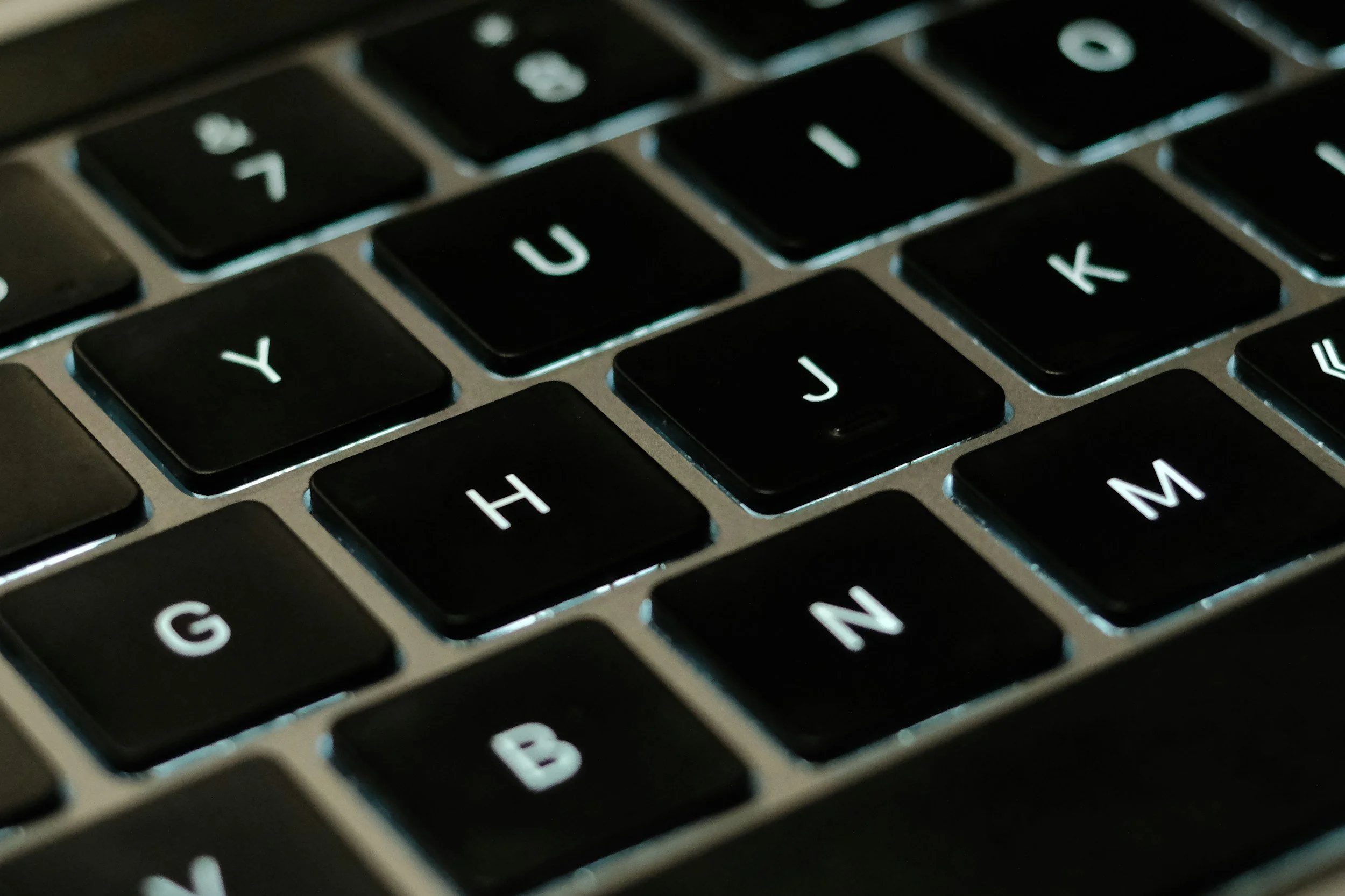 Close-up photo of a computer keyboard with glowing black keys showing letters G, H, J, Y, U, I, K, M, and some punctuation keys.