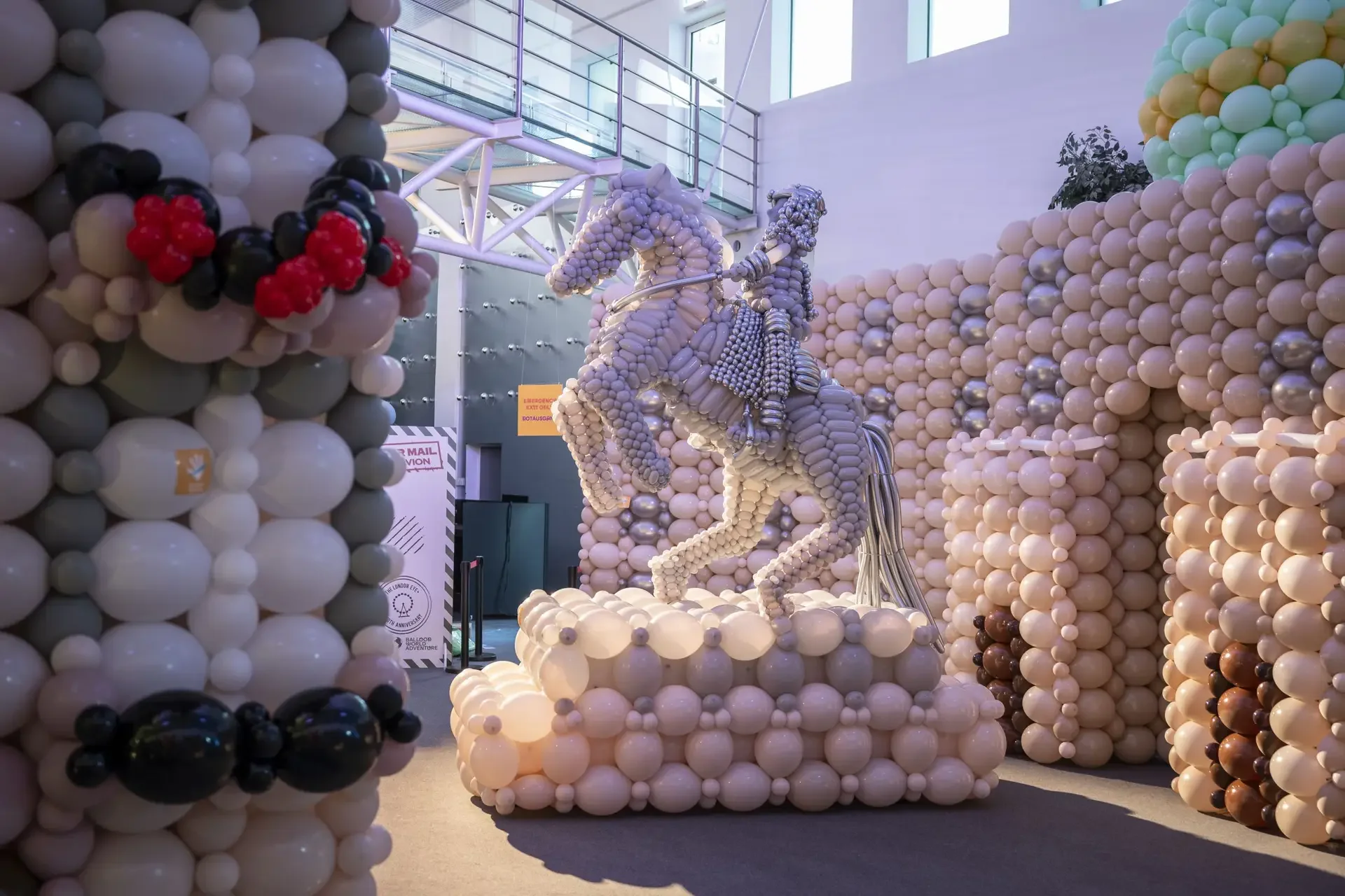 Balloon sculpture of a person riding a horse, constructed with various colored balloons, in an indoor space with high windows.