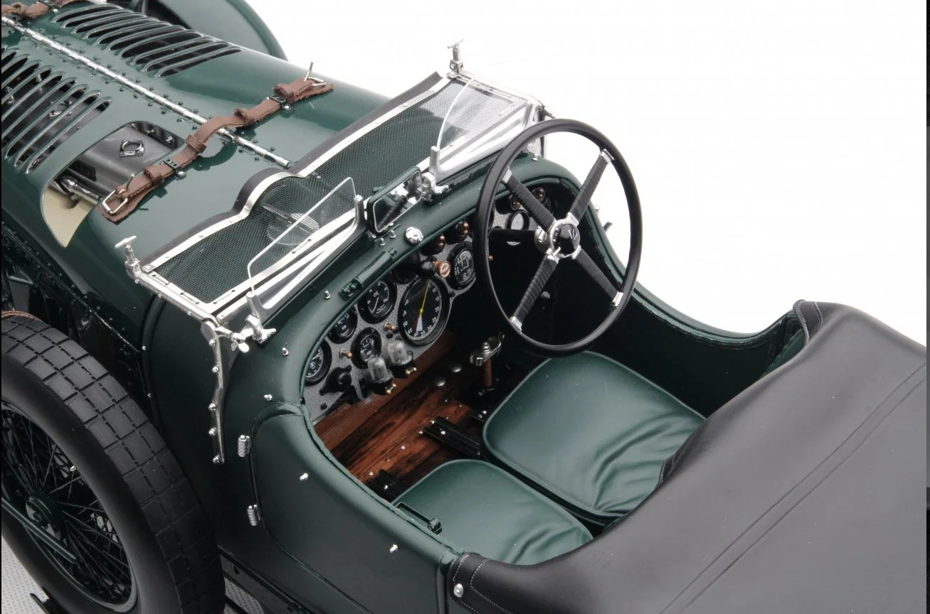 Interior view of a vintage racing car with a green dashboard, leather seats, and a steering wheel, featuring various gauges and metal detailing.