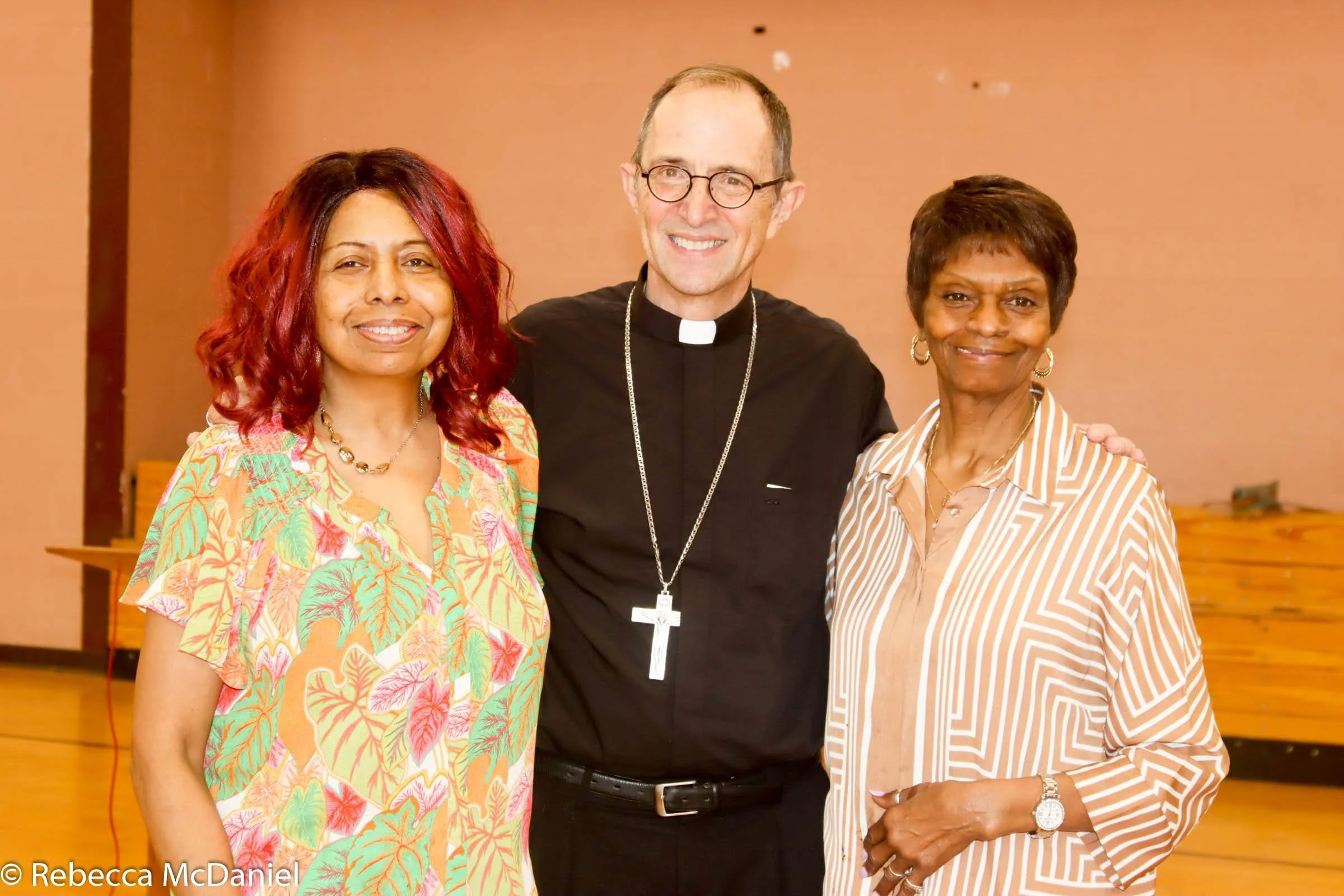 Three women and a priest smiling and standing close together indoors.