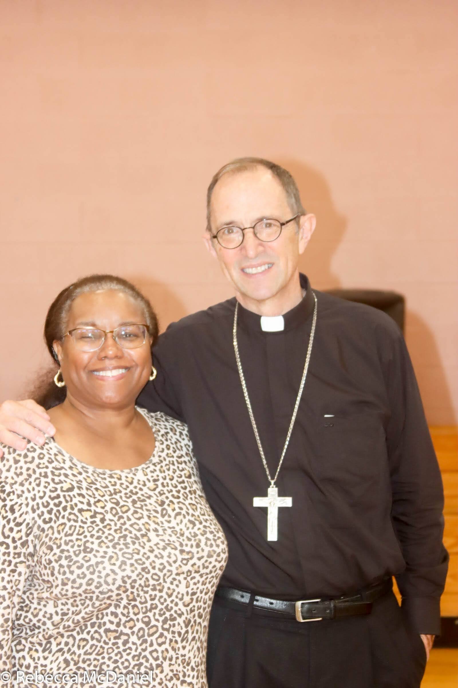 A woman and a priest smiling and standing together indoors.