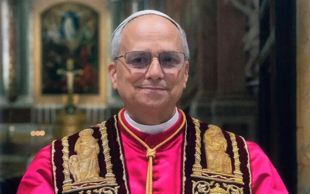 Close-up of a smiling older man in white religious attire, including a white skullcap and a clerical collar.